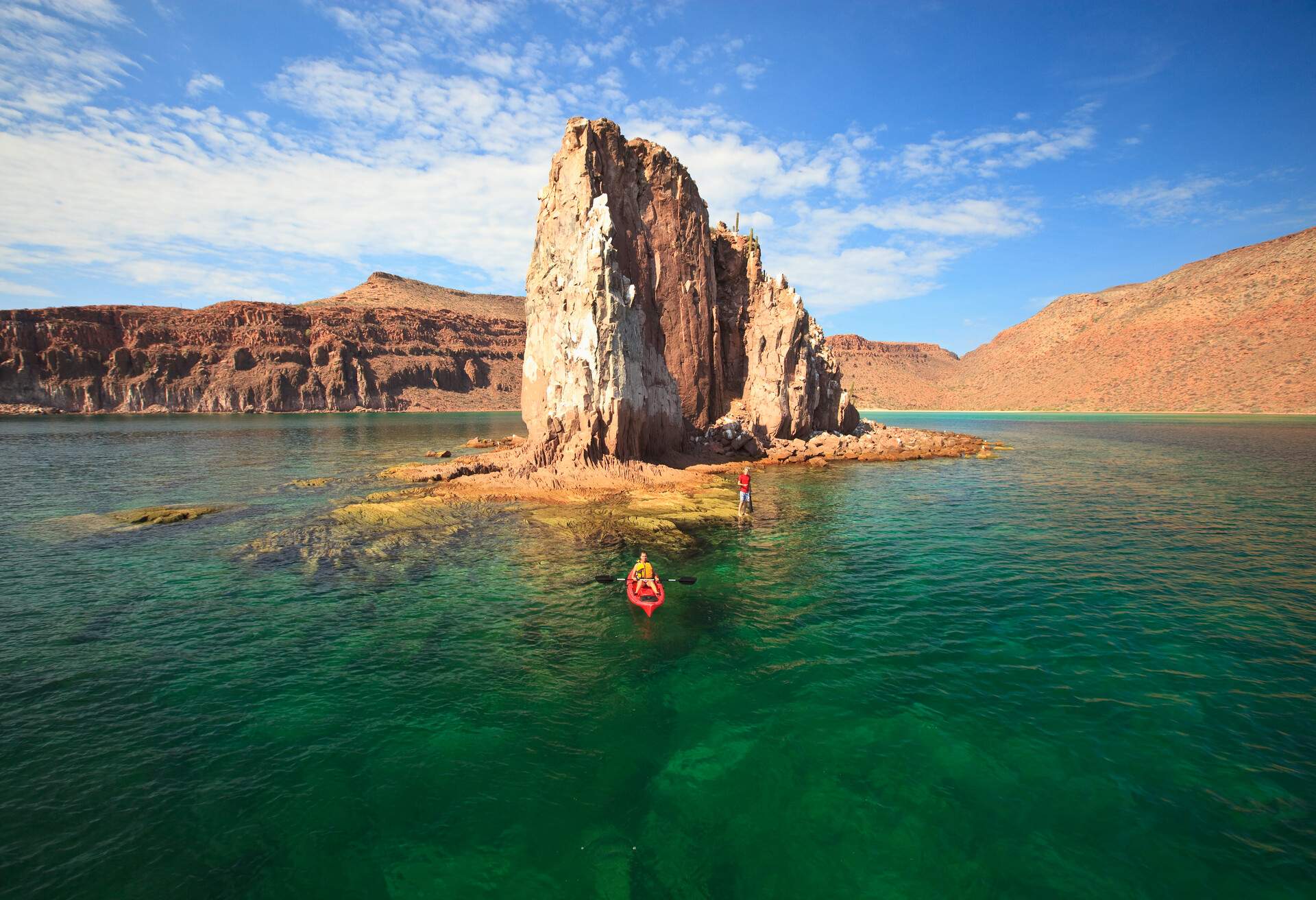 A person in a kayak floating next to a rock formation in the middle of the ocean.