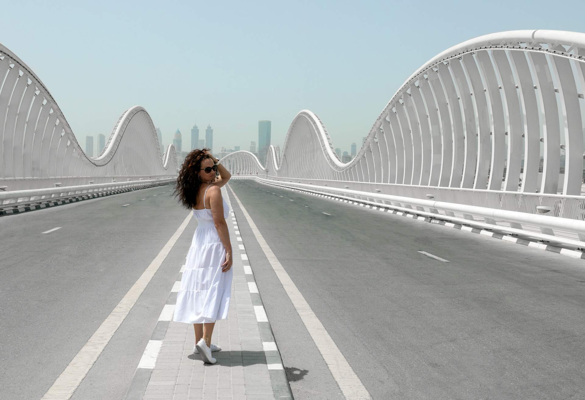 A woman in a white dress poses in the centre of a bridge surrounded by curving safety barriers.