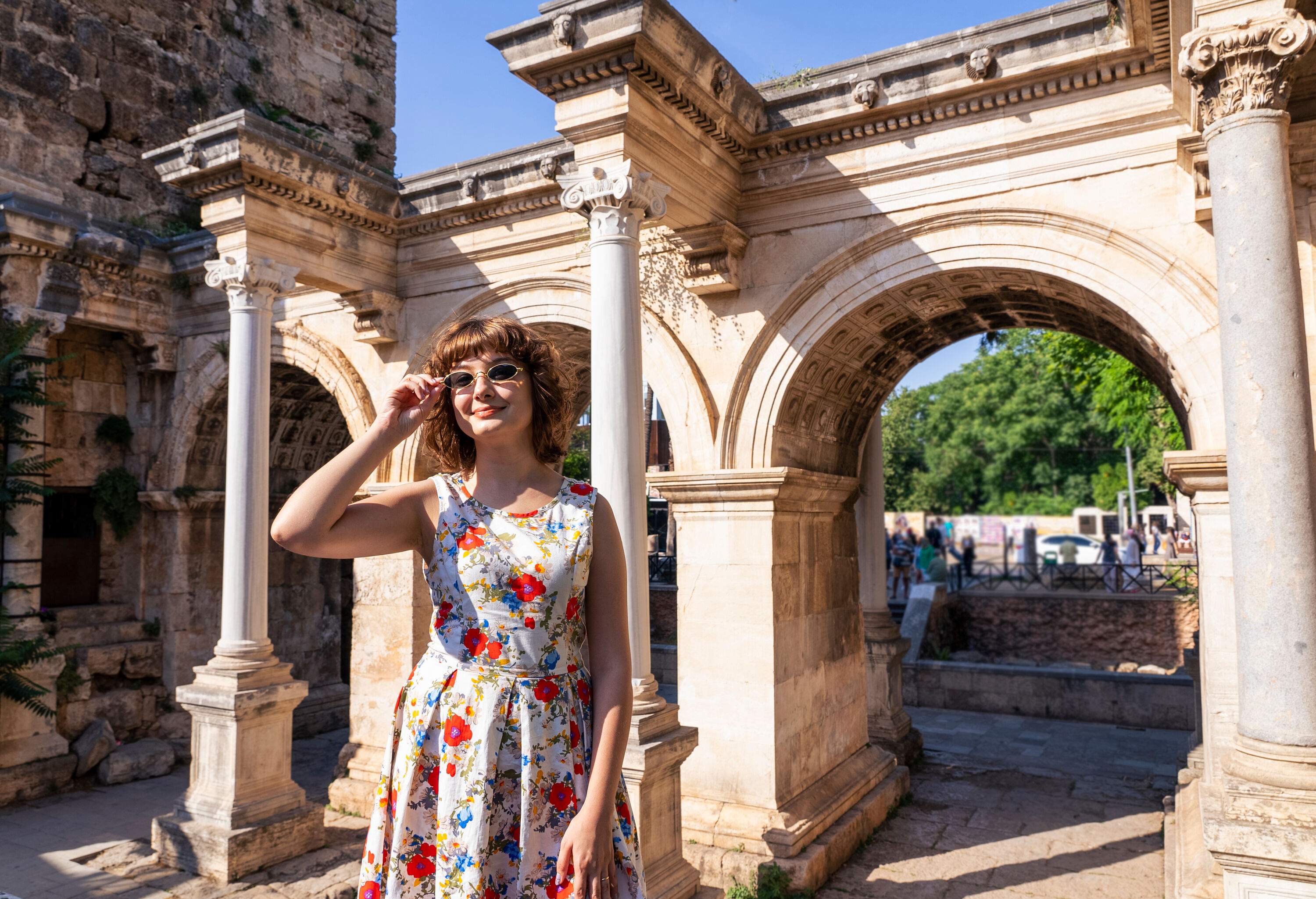 A young woman in a beautiful flowery dress strikes a pose in front of the iconic Antalya Hadrian's Gate.