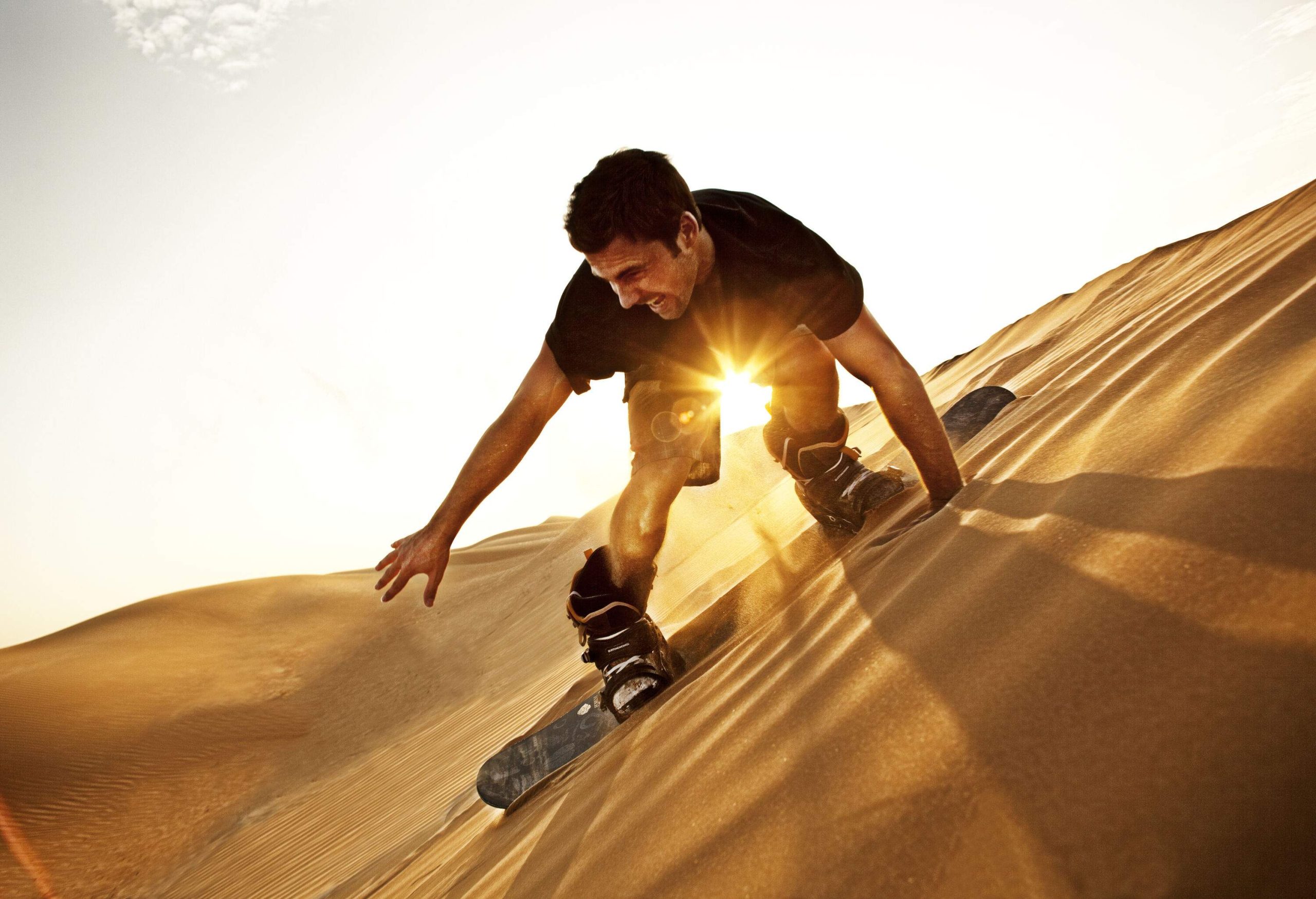 A man descends as he sandboards on the slope of the dunes.