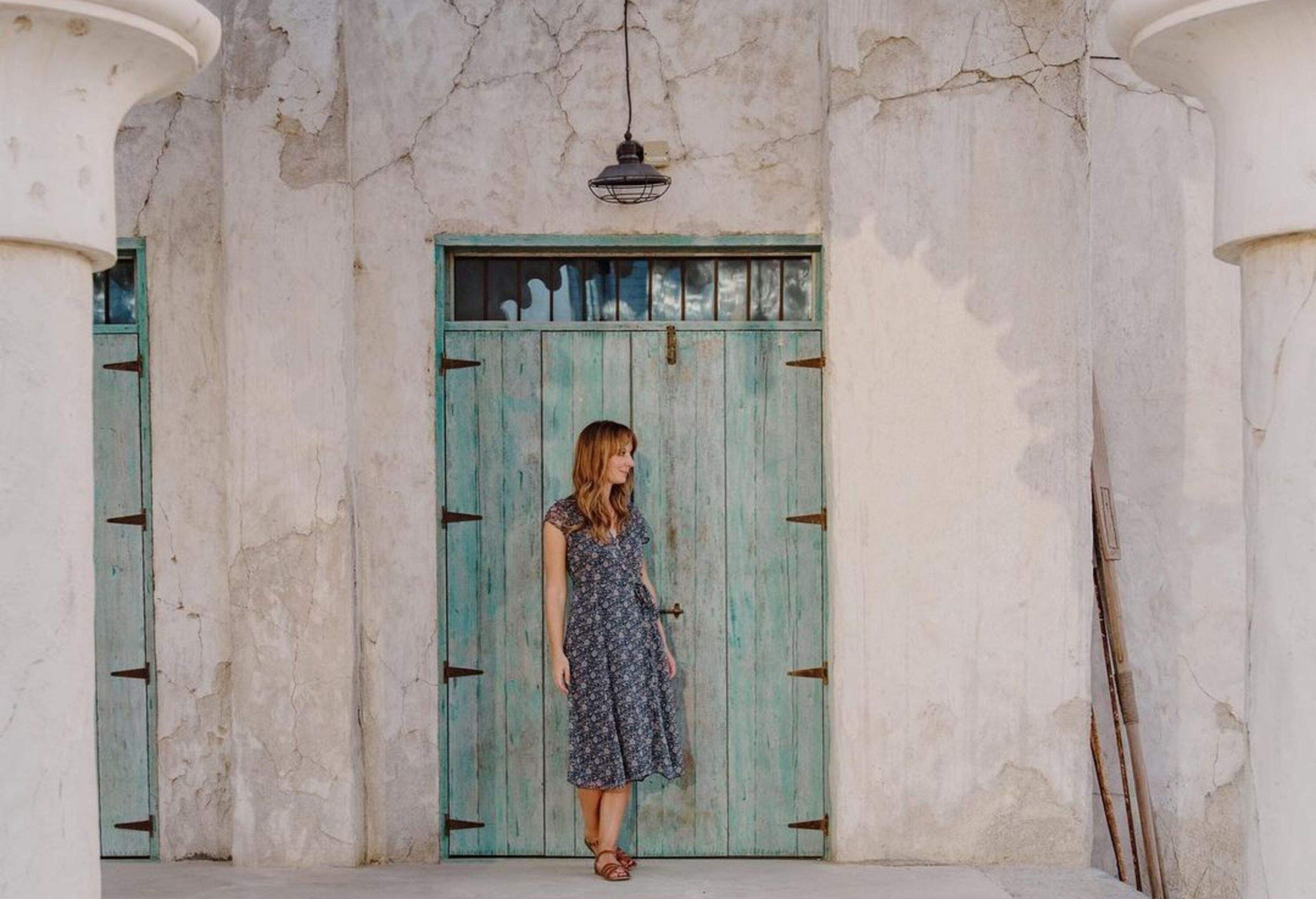 A long-haired blonde woman stands on a light blue wooden door.