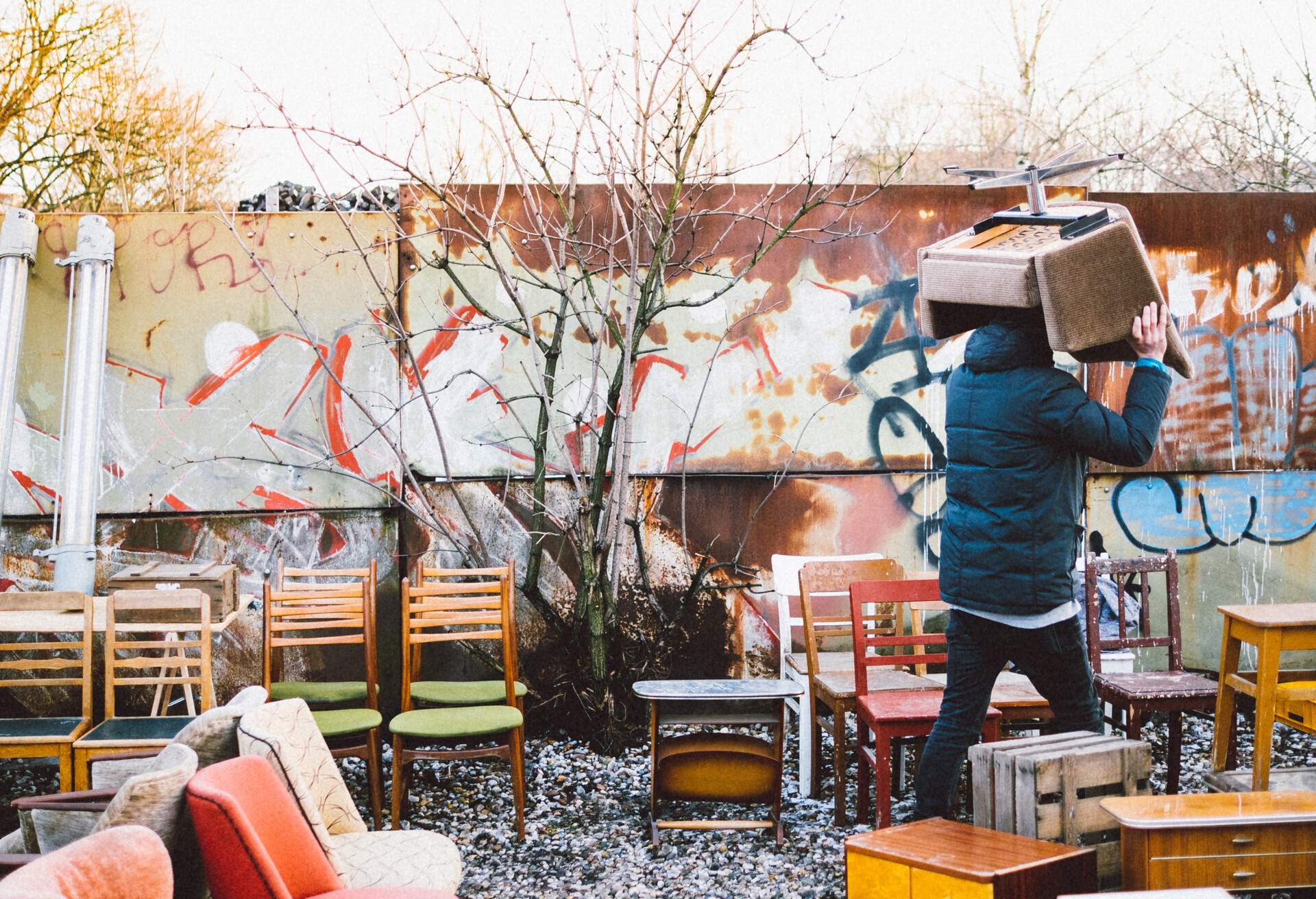 A man at an outdoor furniture store carrying a chair over his head.