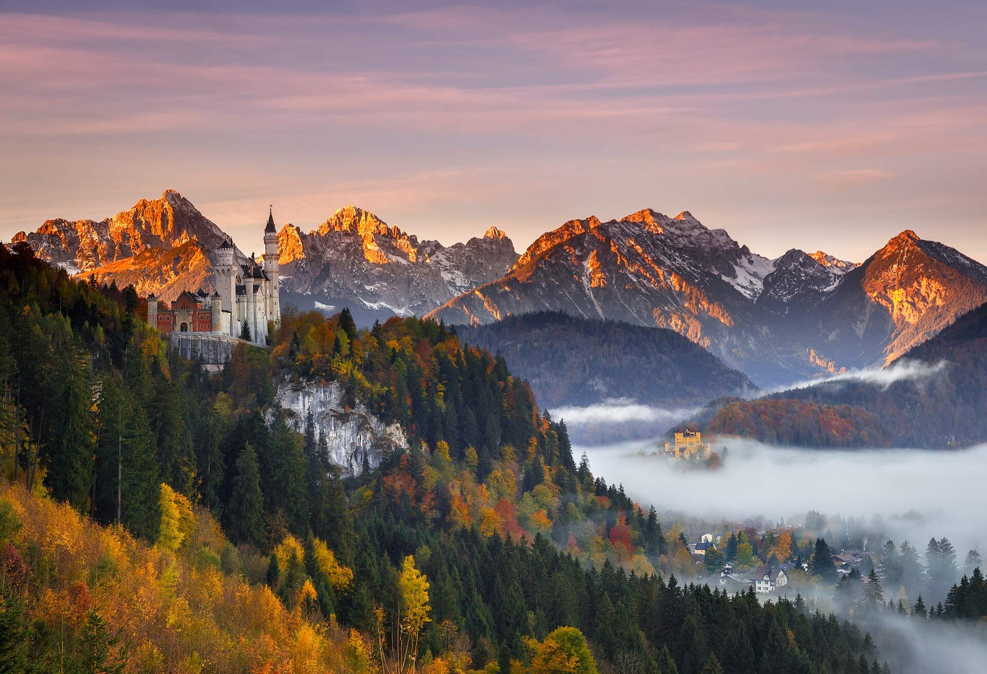 A castle on a mountaintop with views of the snow-capped mountains and the foggy village below.