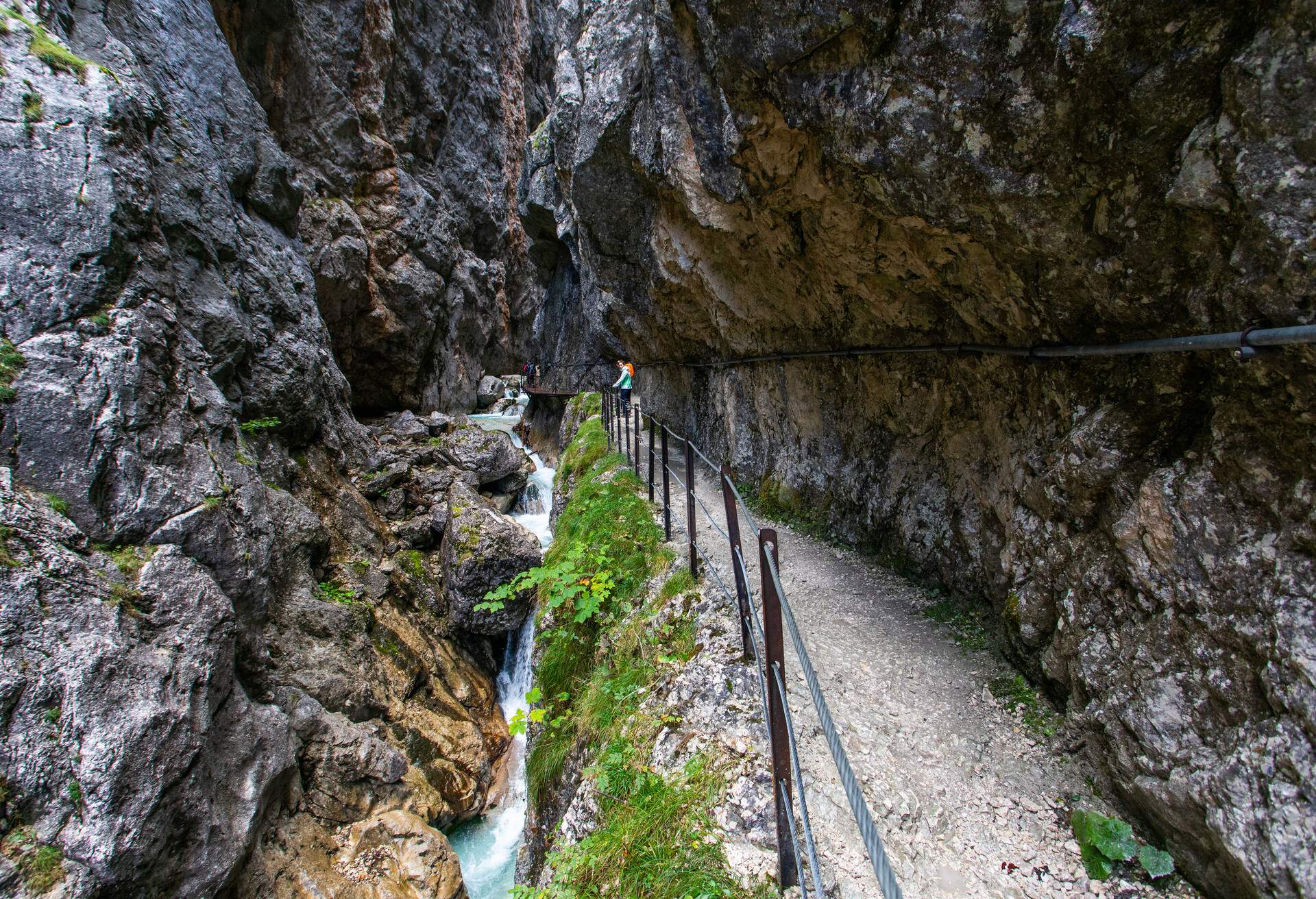 A hiking trail carved into the side of rock mountains with a waterfall tumbling over the gorge below.