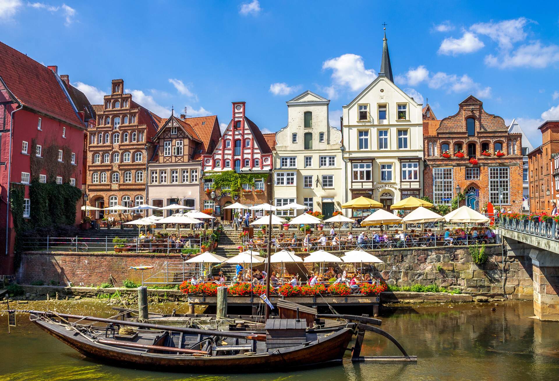 A moored boat along a promenade with an outdoor cafe in front of row dwellings, Stintmarket, Lueneburg