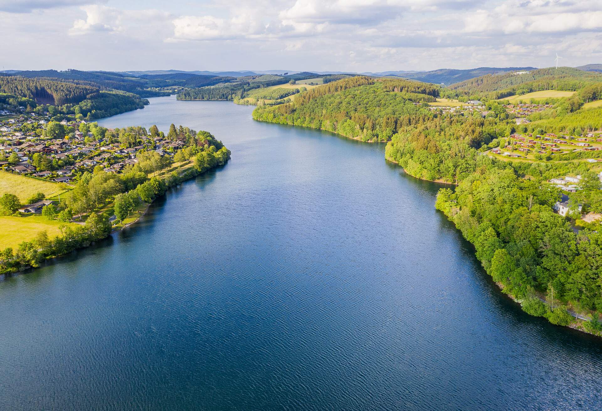 A large lake surrounded by a lakeside village and meadows covered in dense forest.