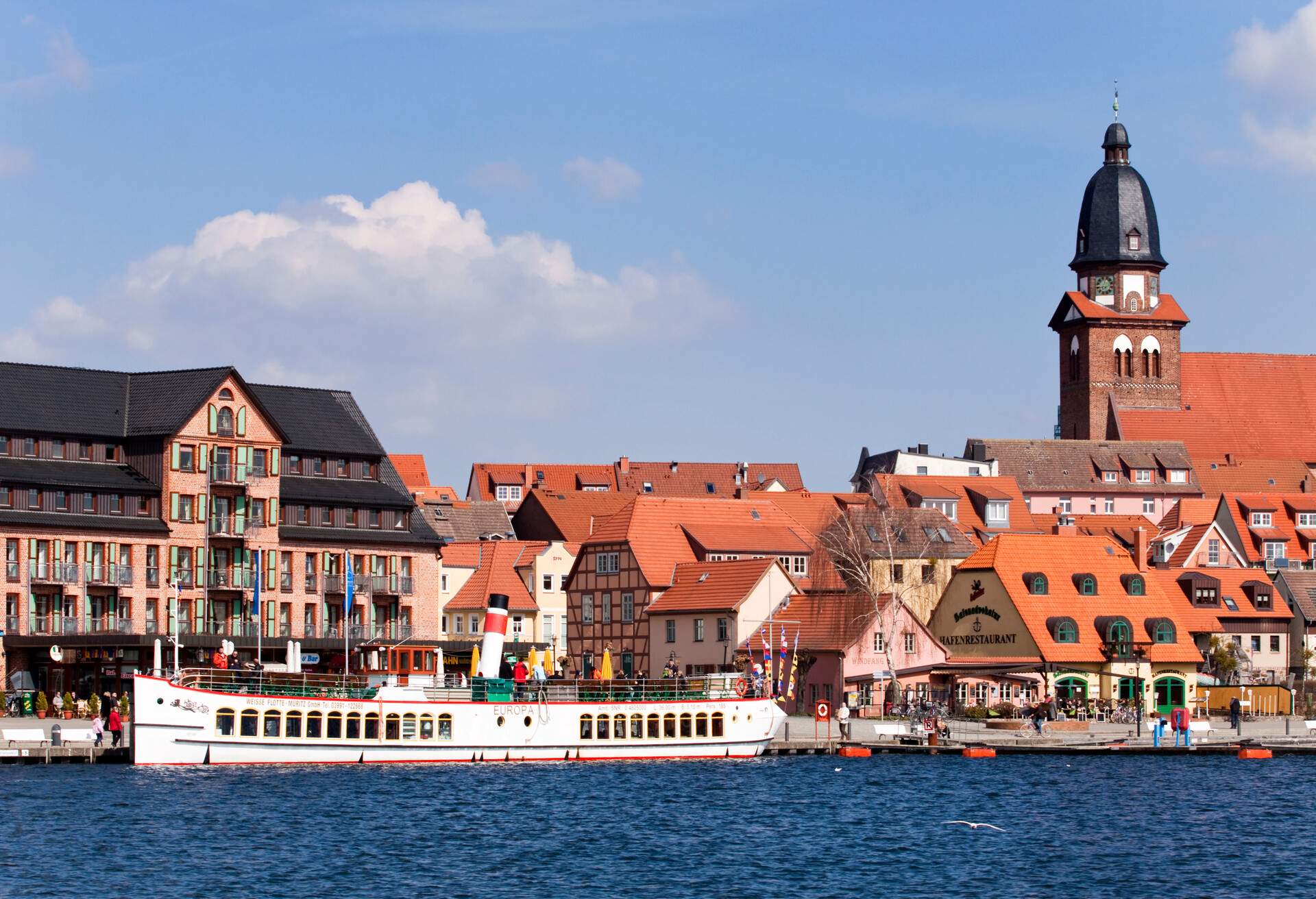 A long boat moored in a port with a charming historic centre that features a variety of traditional architecture, including half-timbered houses and red brick buildings.