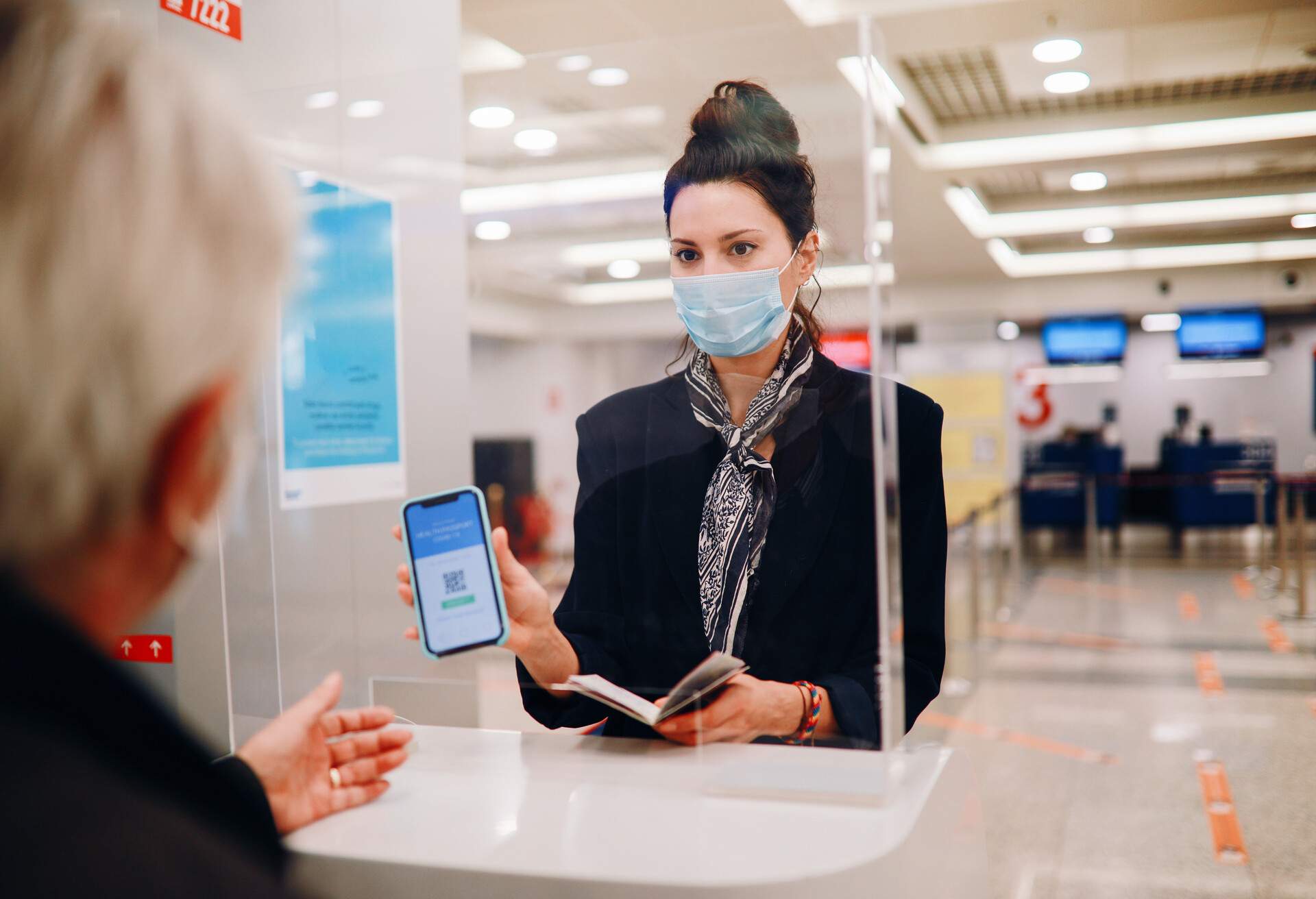 A woman with a facemask shows her mobile phone with a QR code.