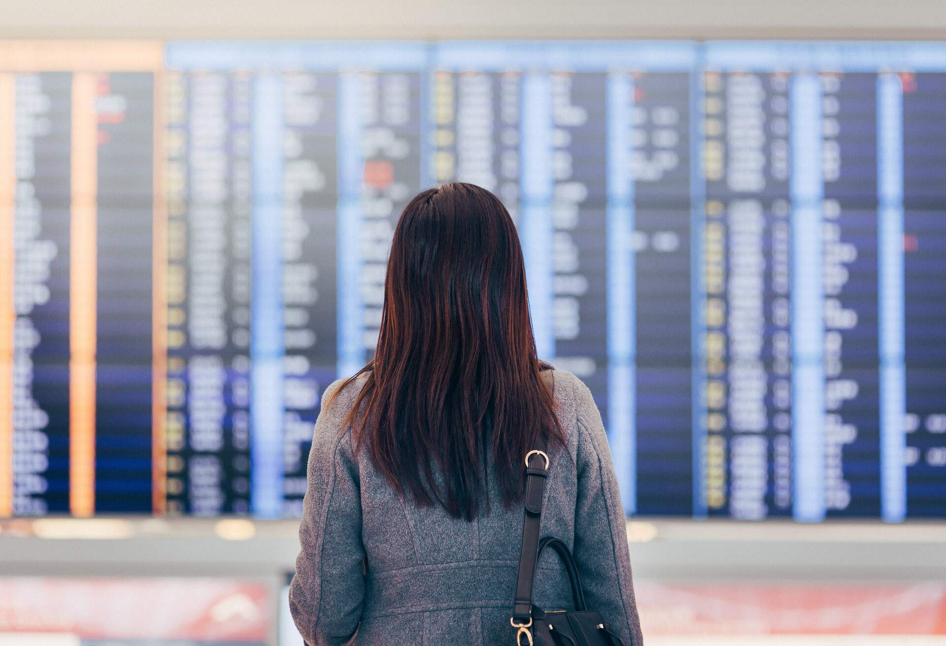 A woman is standing in an airport terminal, looking up at the Arrival Departure Board.