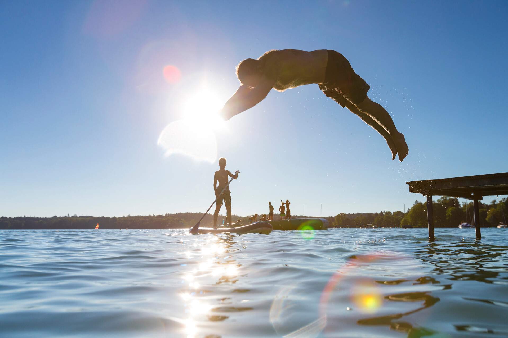 A man diving into a lake with kids enjoying water activities in the distance.
