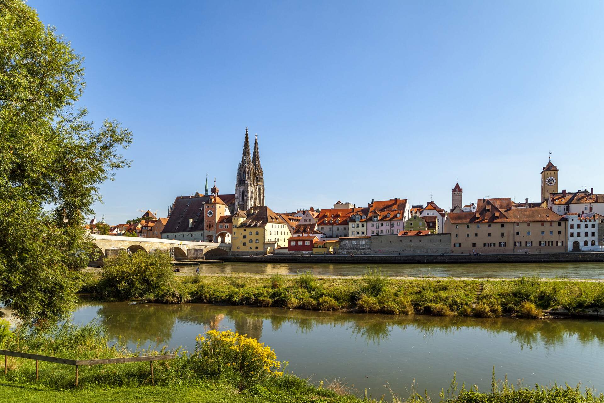 An arch stone bridge across a broad river heading towards a gothic church surrounded by a compact cluster of houses.