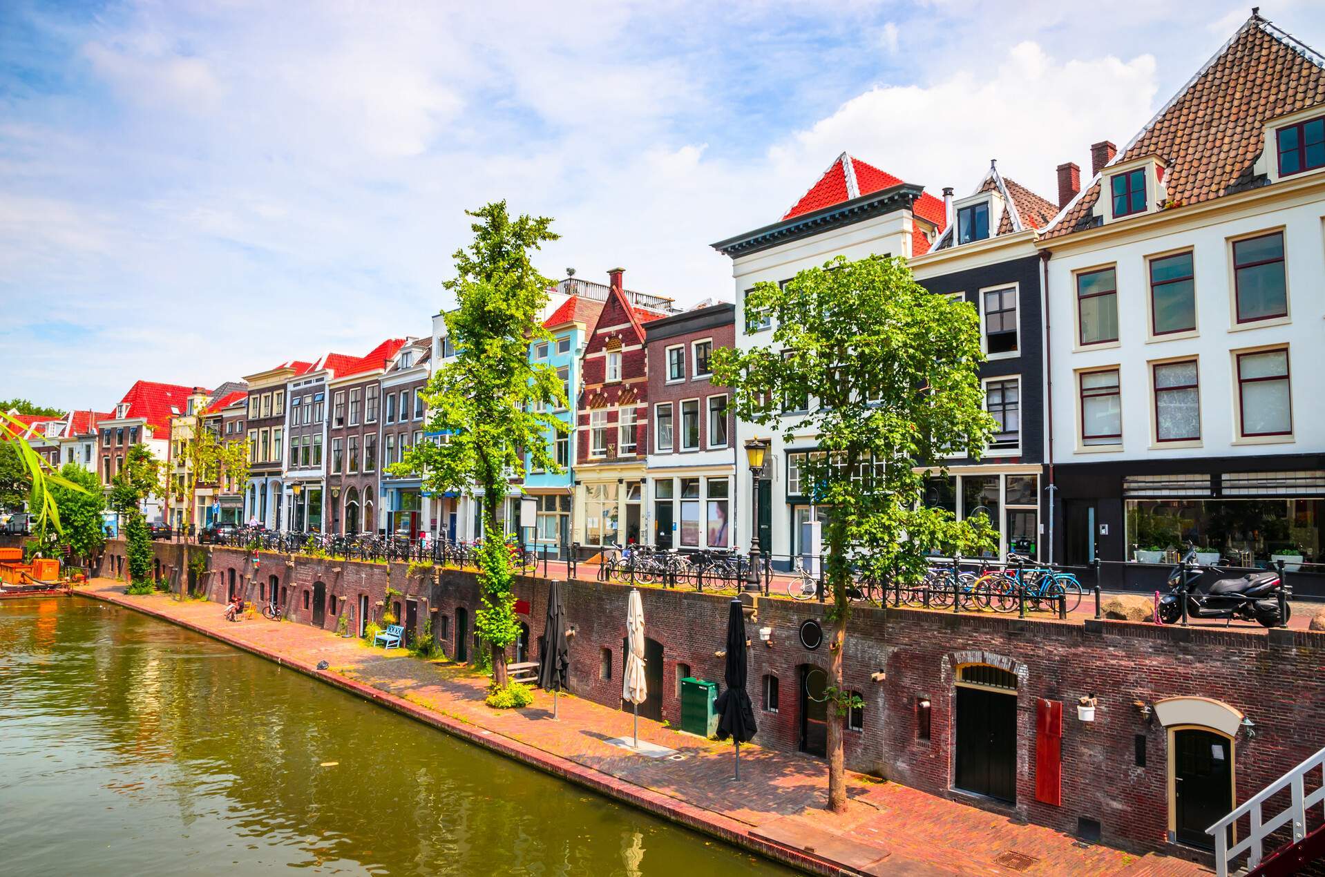 A water canal across a promenade with parked bicycles and a row of colourful adjacent buildings.