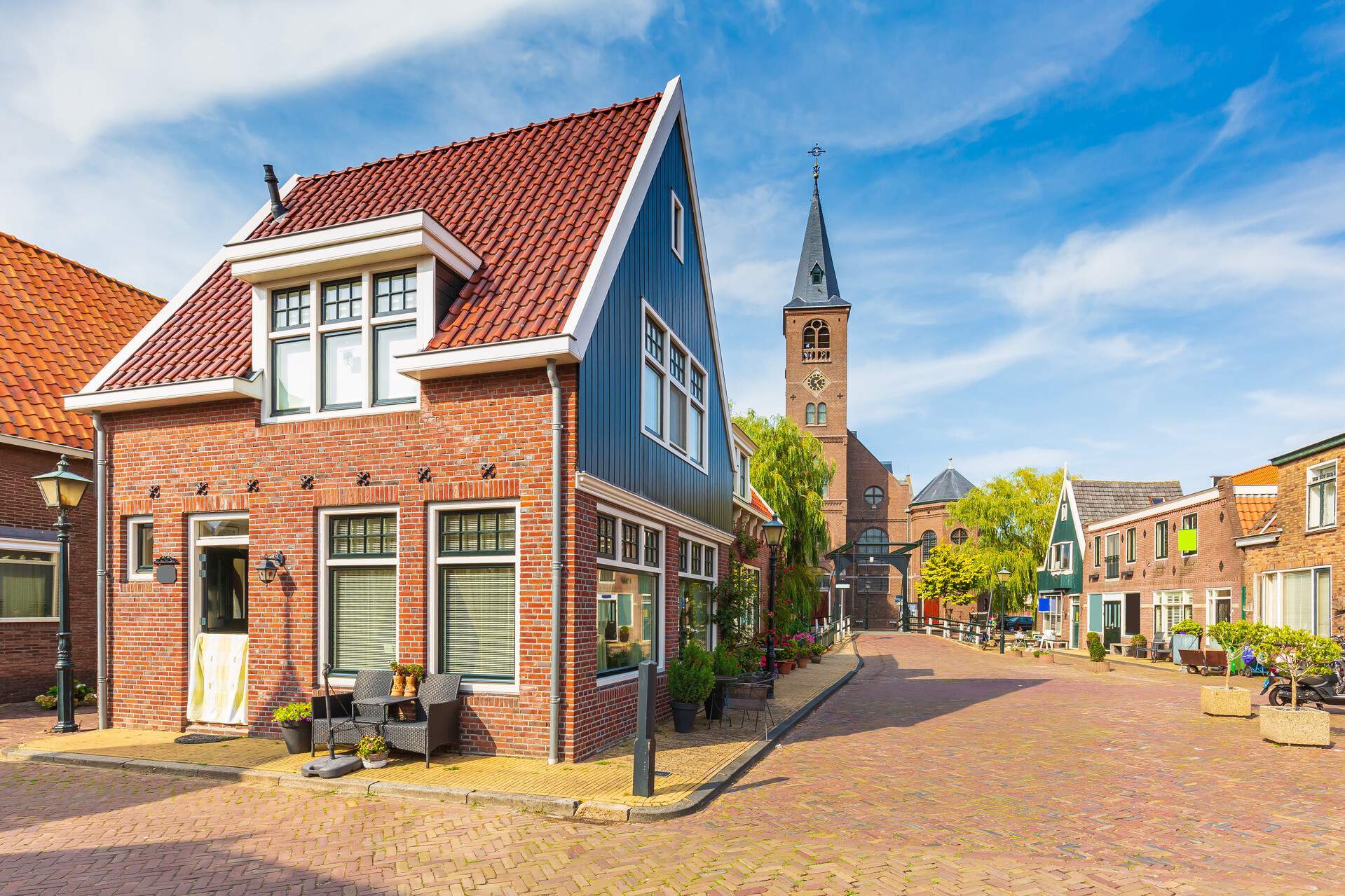 A church with an imposing tower lies at the end of a brick road between colourful traditional houses.