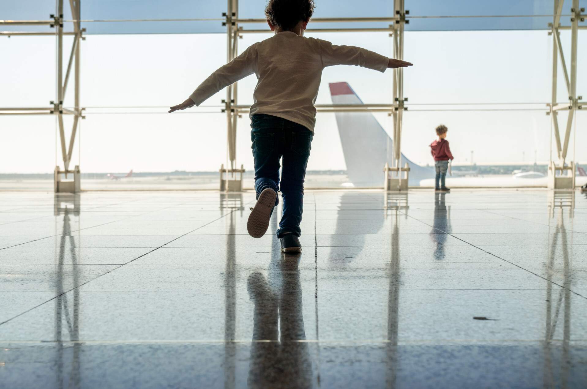 A kid running in the airport with his arms stretched like airplane wings