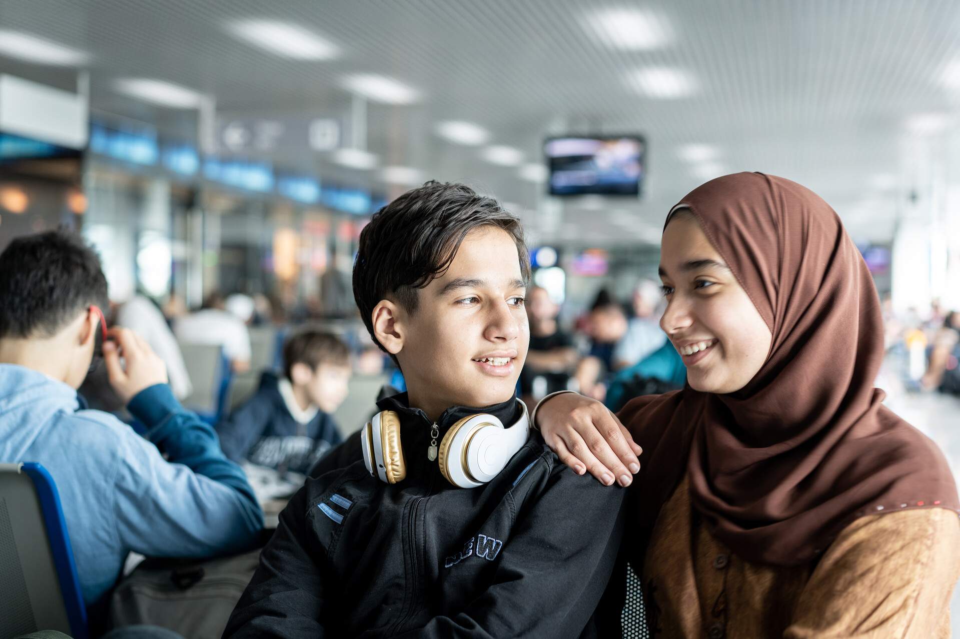 Two teenagers sitting in an airport terminal.
