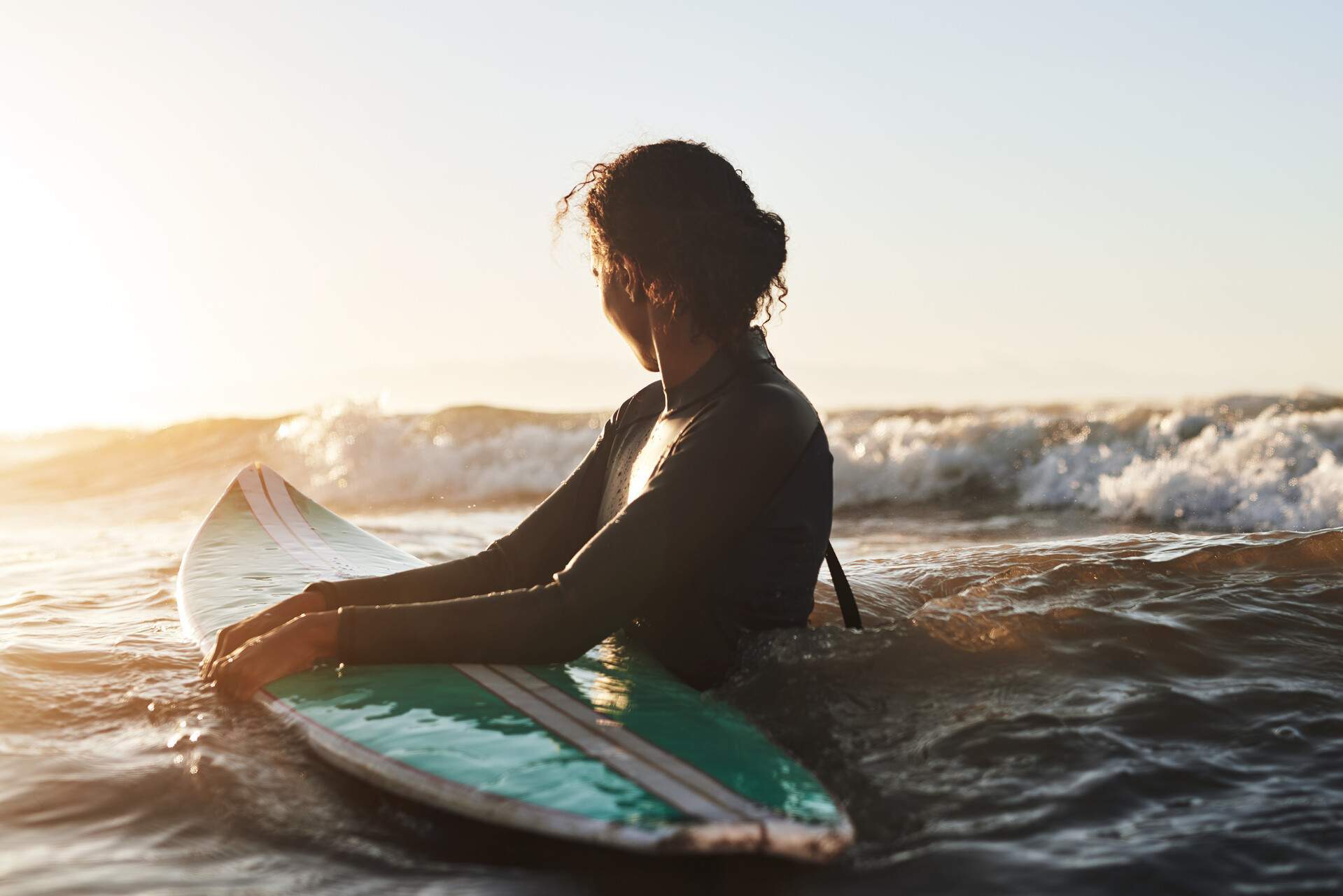 A woman holding on to her surfboard in the sea, with rising waves in the background.