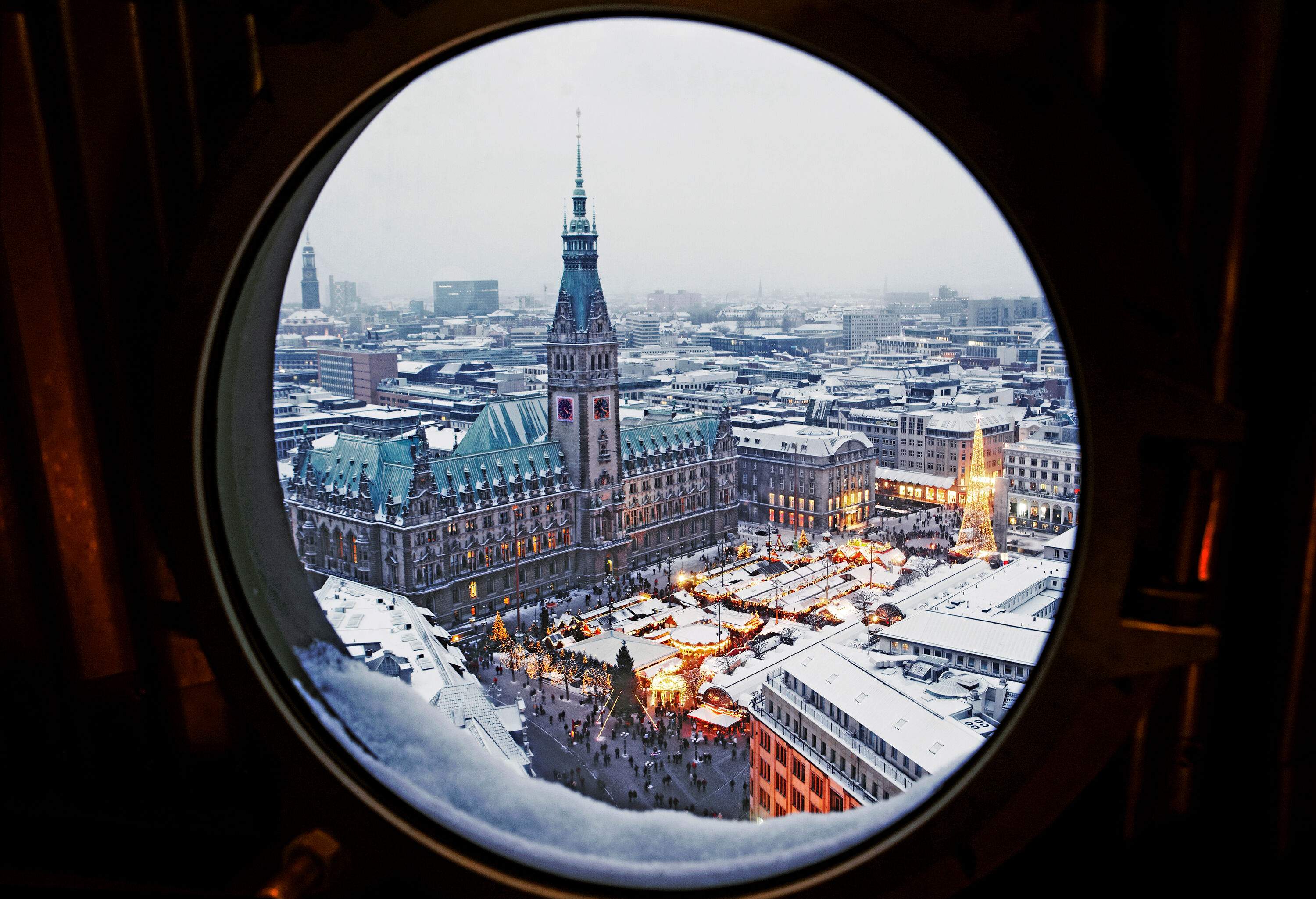 A marketplace illuminated by dazzling Christmas lights from a porthole window.