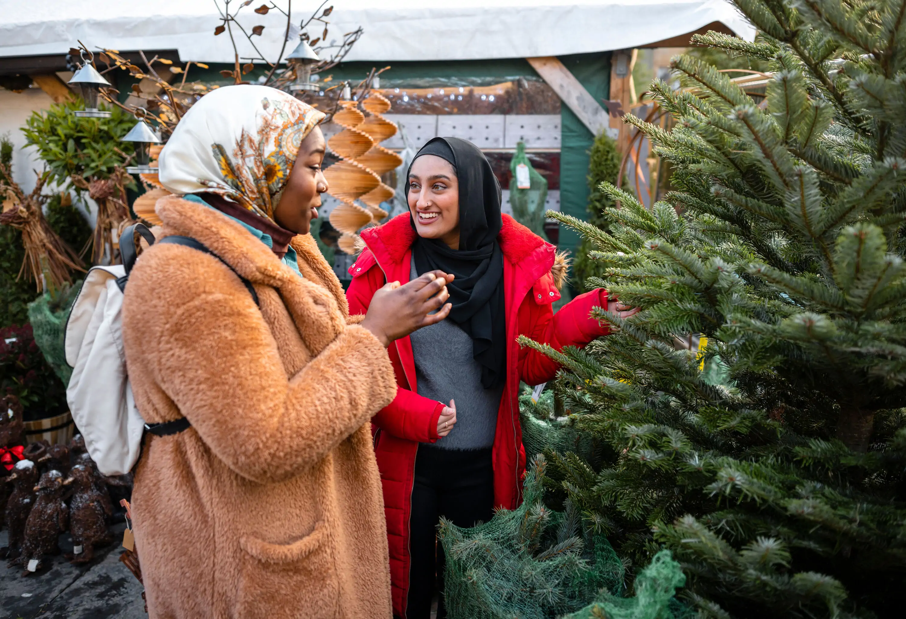 Two women chatting happily while shopping for a Christmas tree.