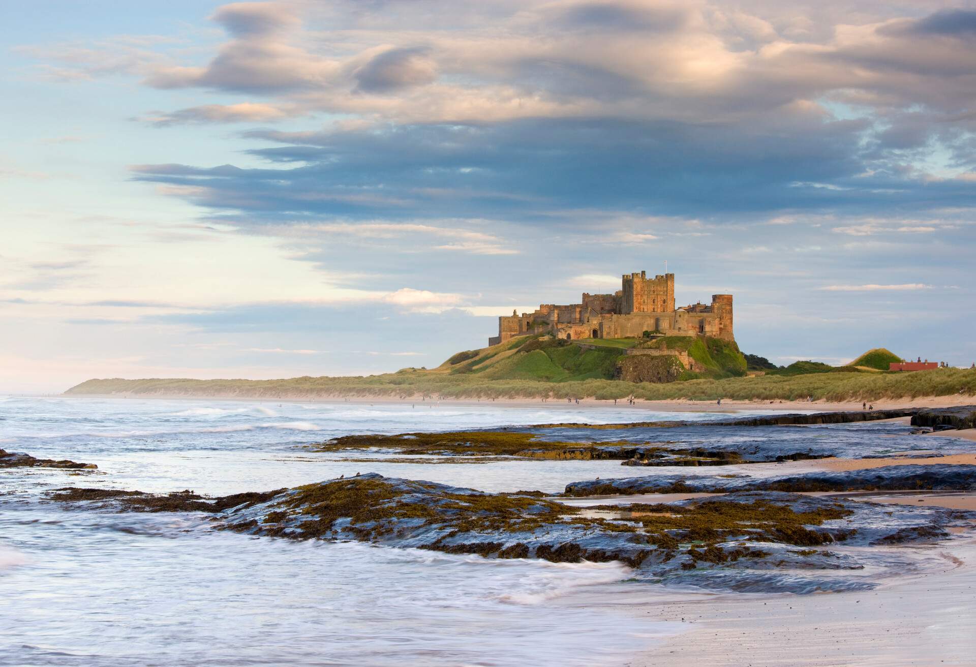 A vast castle crowned on a hill alongside a rugged coast surrounded by the big waves of the sea.