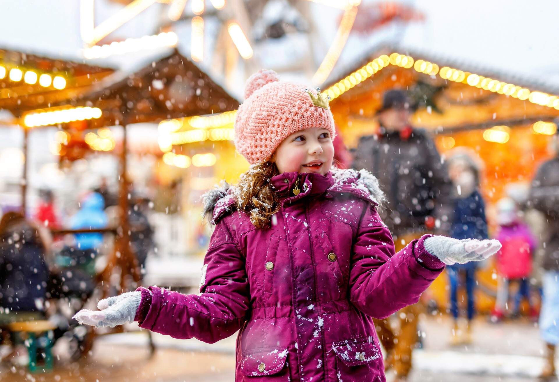 Little cute kid girl having fun on traditional German Christmas market during strong snowfall.. Happy child enjoying traditional family market in Germany, Frankfurt. Laughing girl in colorful clothes.