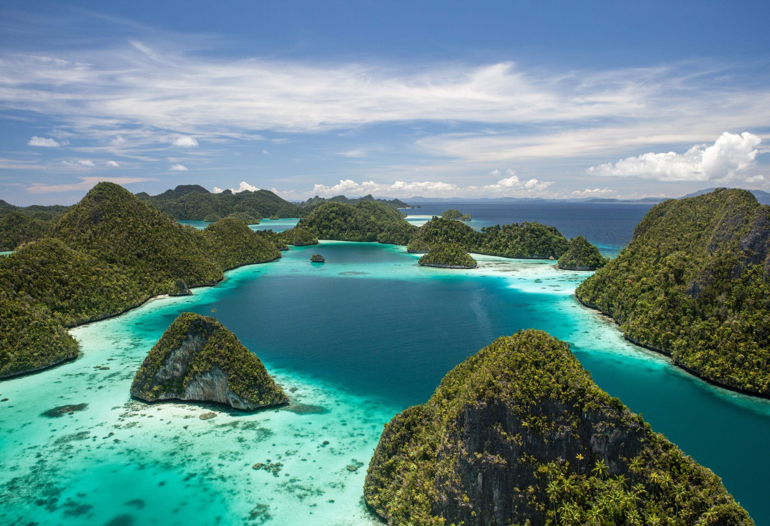 A group of islands of various sizes protrudes from the shallow, crystal clear, tranquil waters.