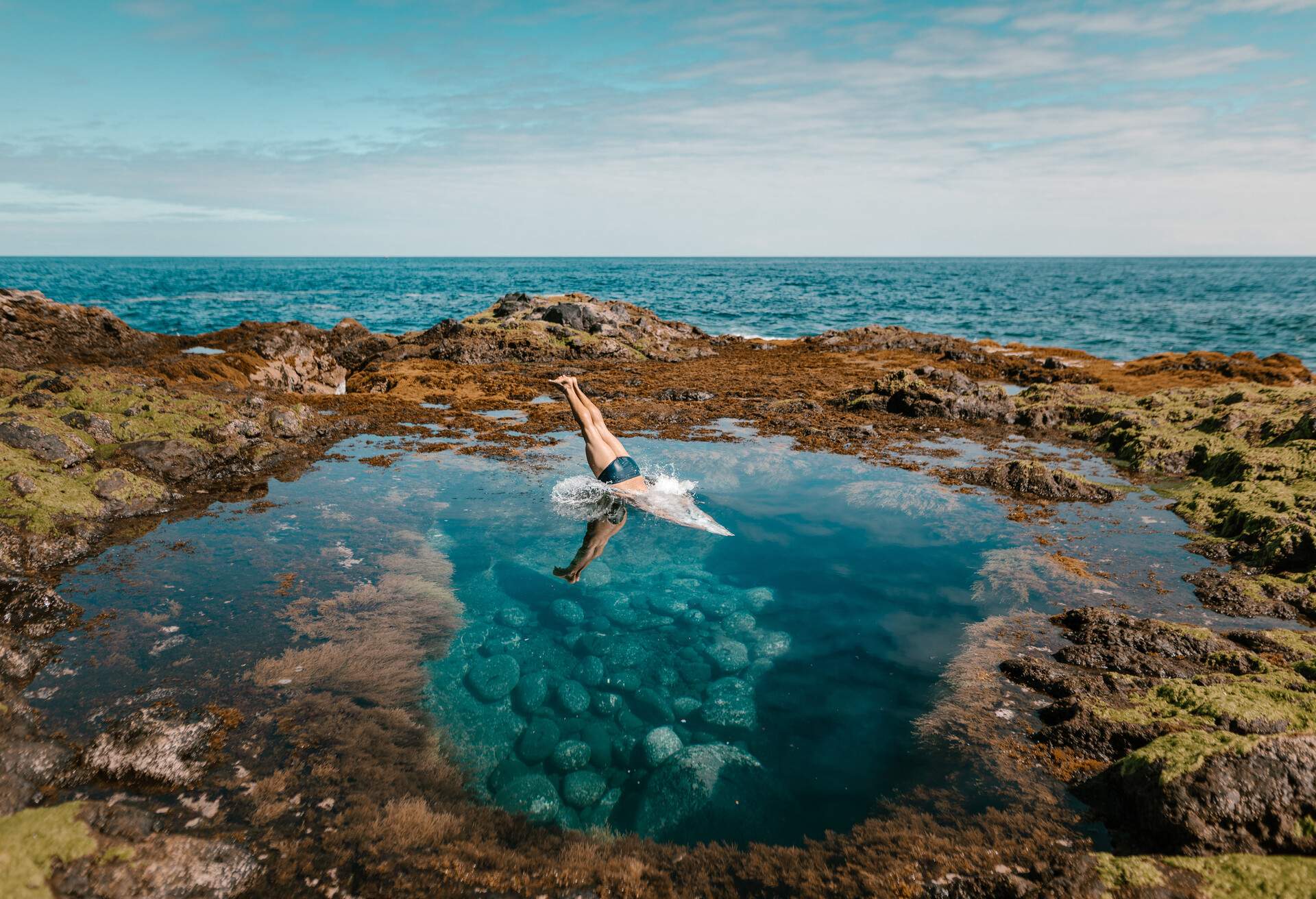 A male tourist dive into the natural turquoise pool alongside the ocean.