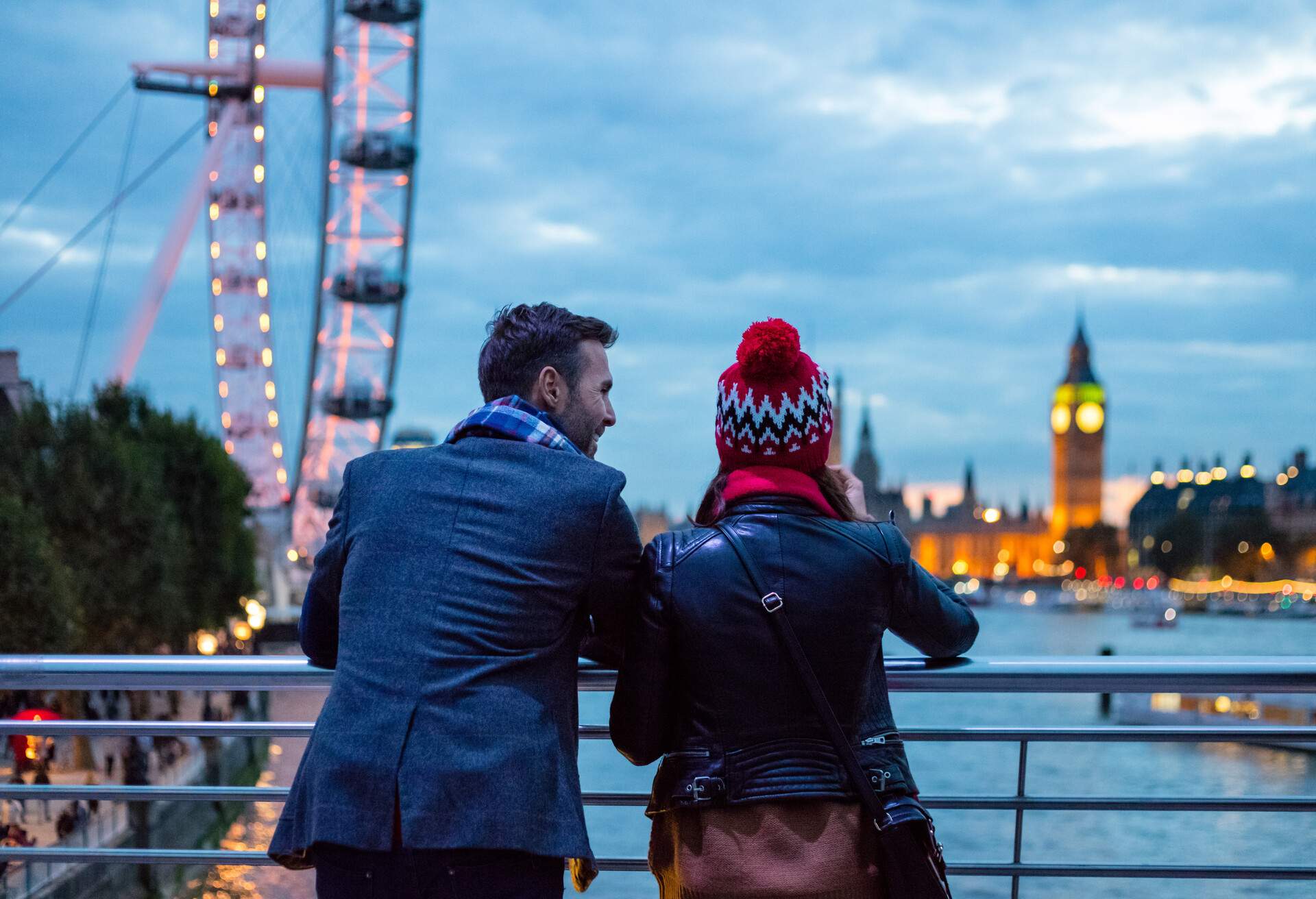 A couple enjoying the nighttime view of the city's attractions as they lean on a railing.