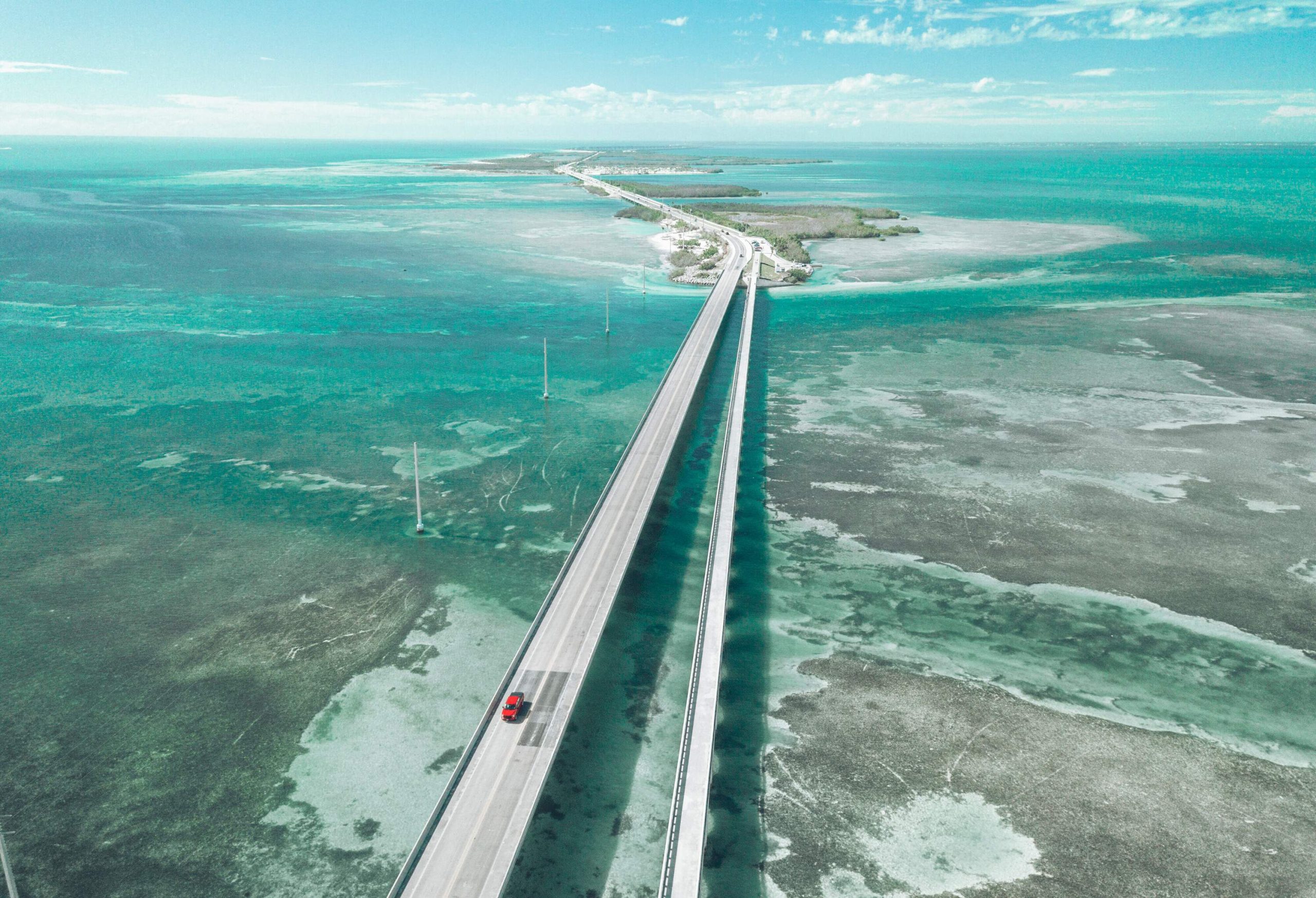 A lone car travels down a road bridge across a wide ocean.