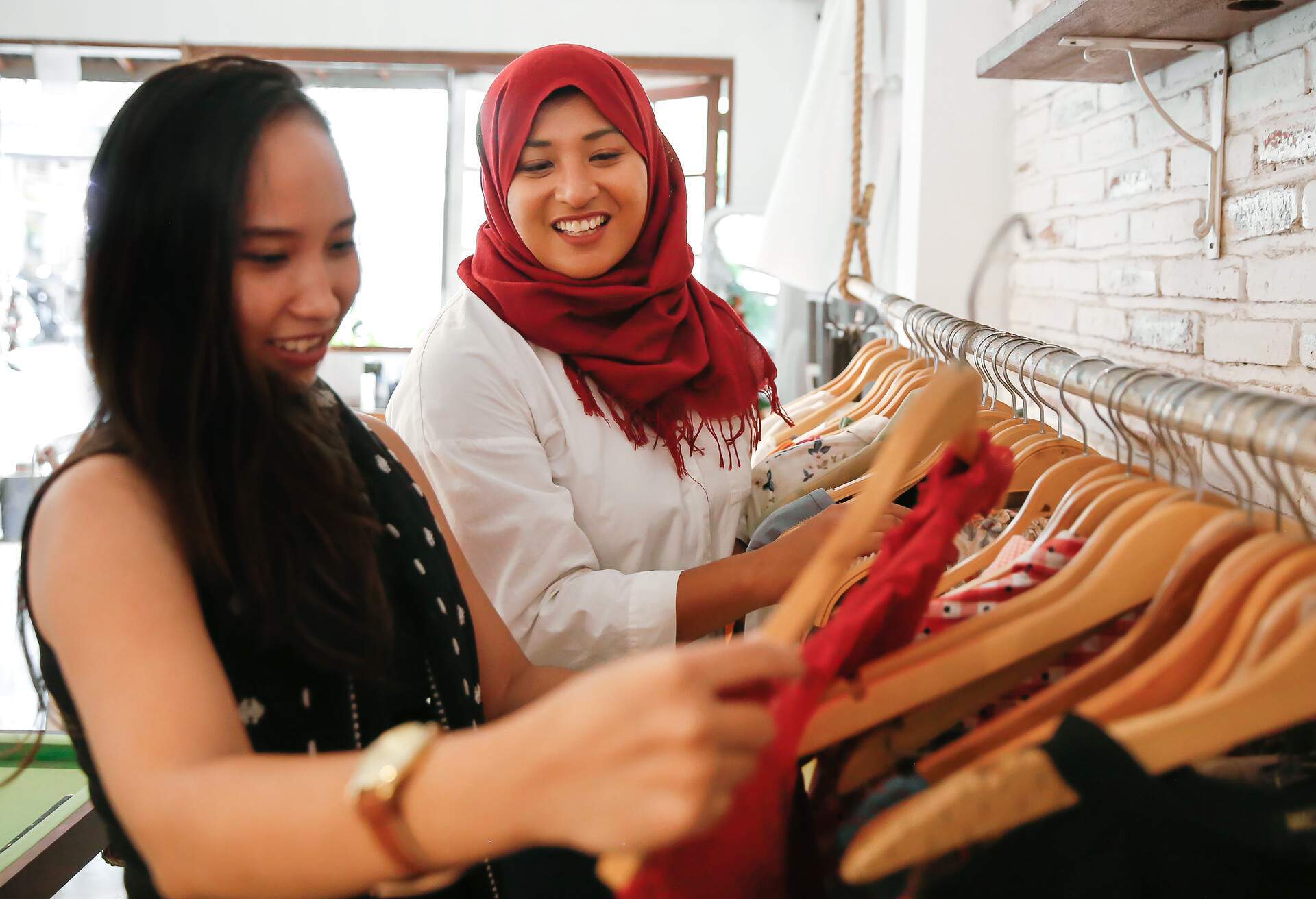 Two happy female friends inside a boutique shopping for clothes.