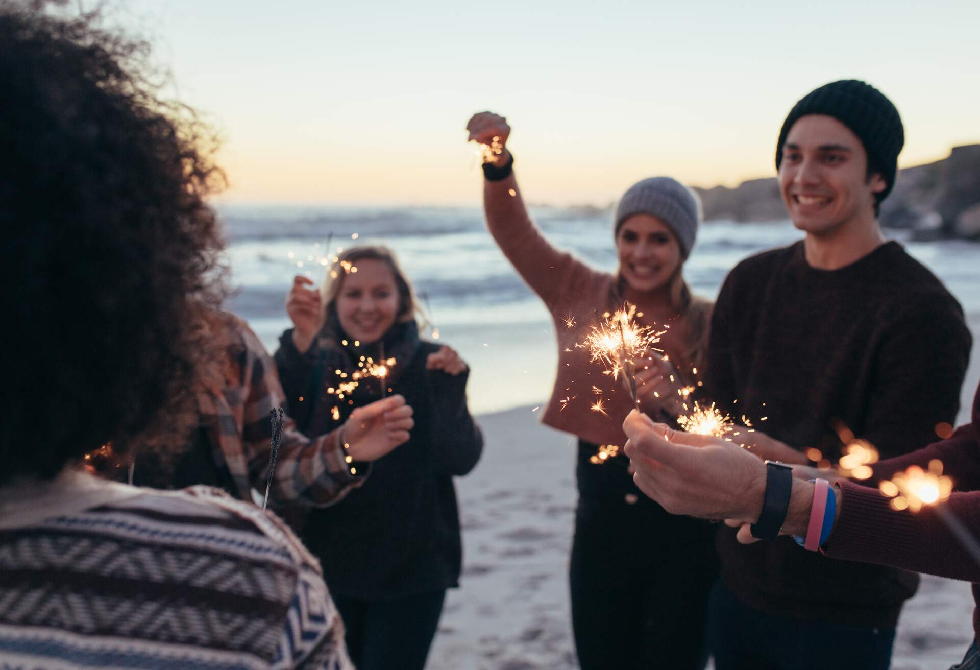 Group of people holding sparkling sparklers at the beach.