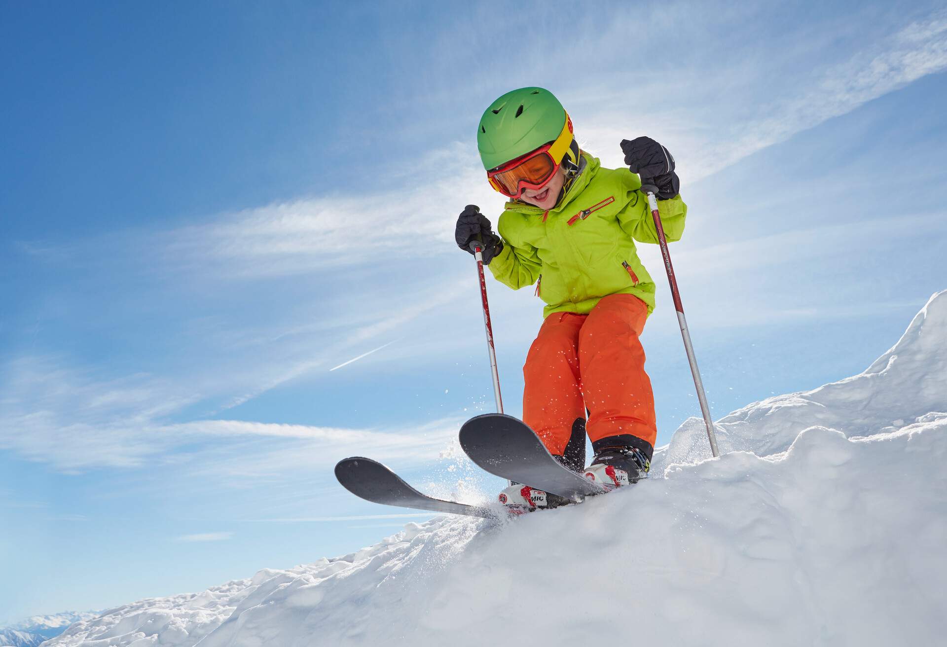 A smiling little girl with thick clothes glides along the snow under a clear blue sky.