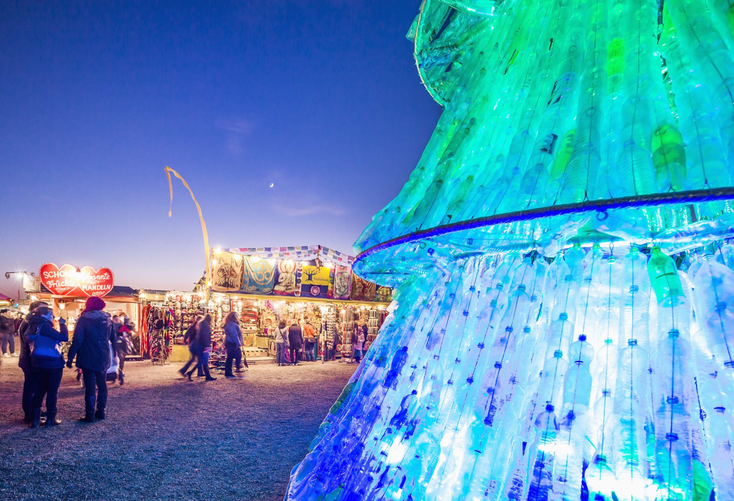 A Christmas tree made from discarded bottles strung together and surrounded by seasonal stores.