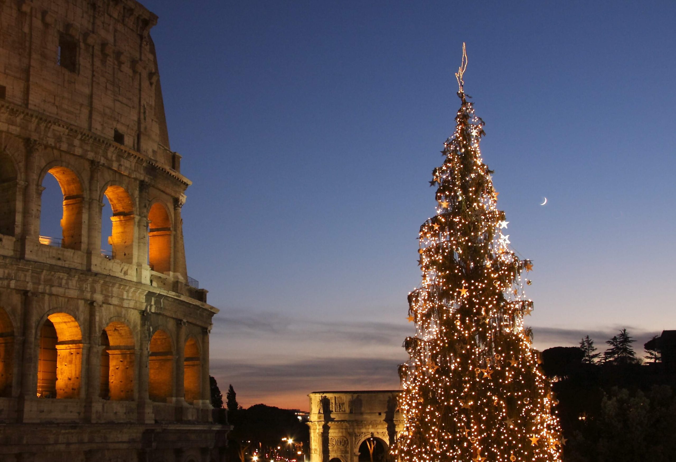 A tall Christmas tree decorated with bright lights next to the illuminated ruins of the Coliseum in Rome, Italy.