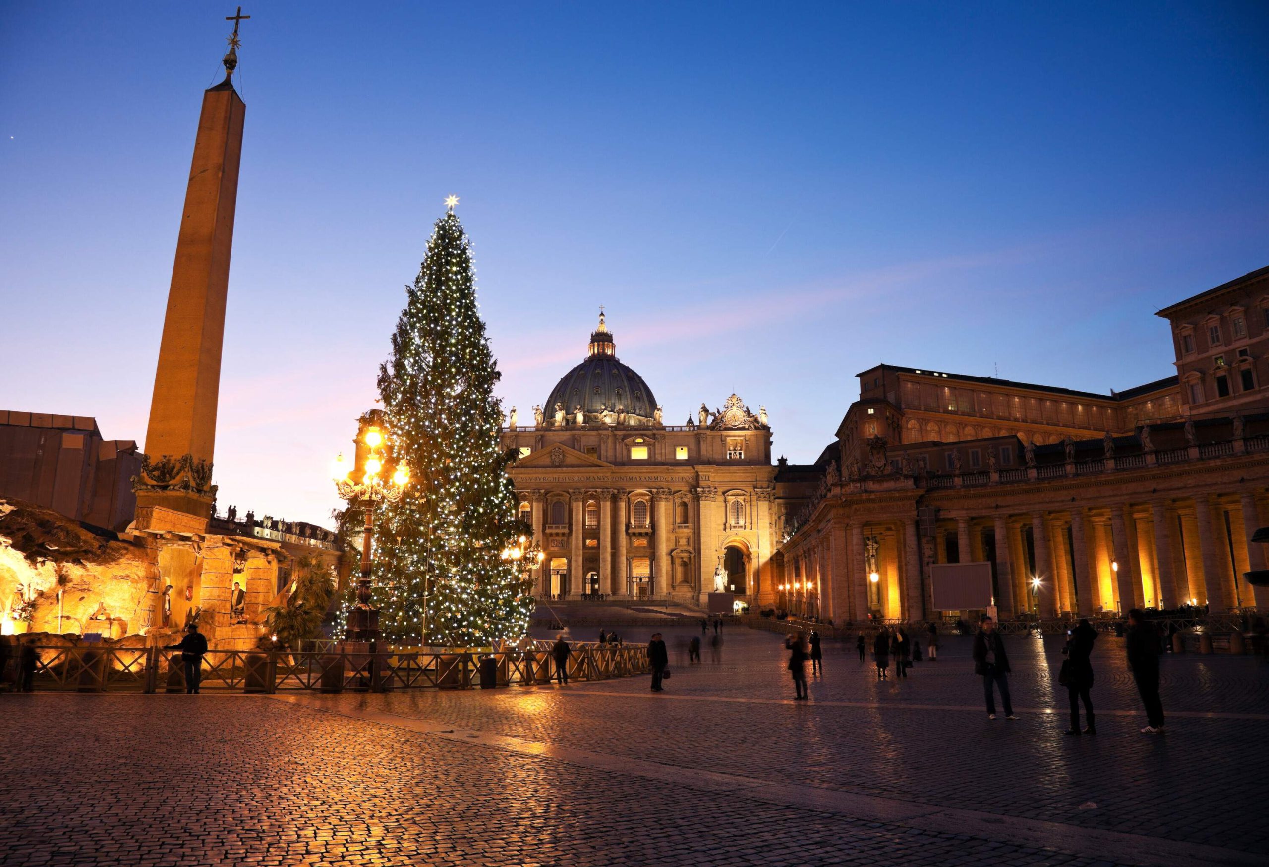 A giant lit Christmas tree adjacent to an ancient Egyptian obelisk in Saint Peter's Square overlooking St. Peter's Basilica in Rome, Vatican City.