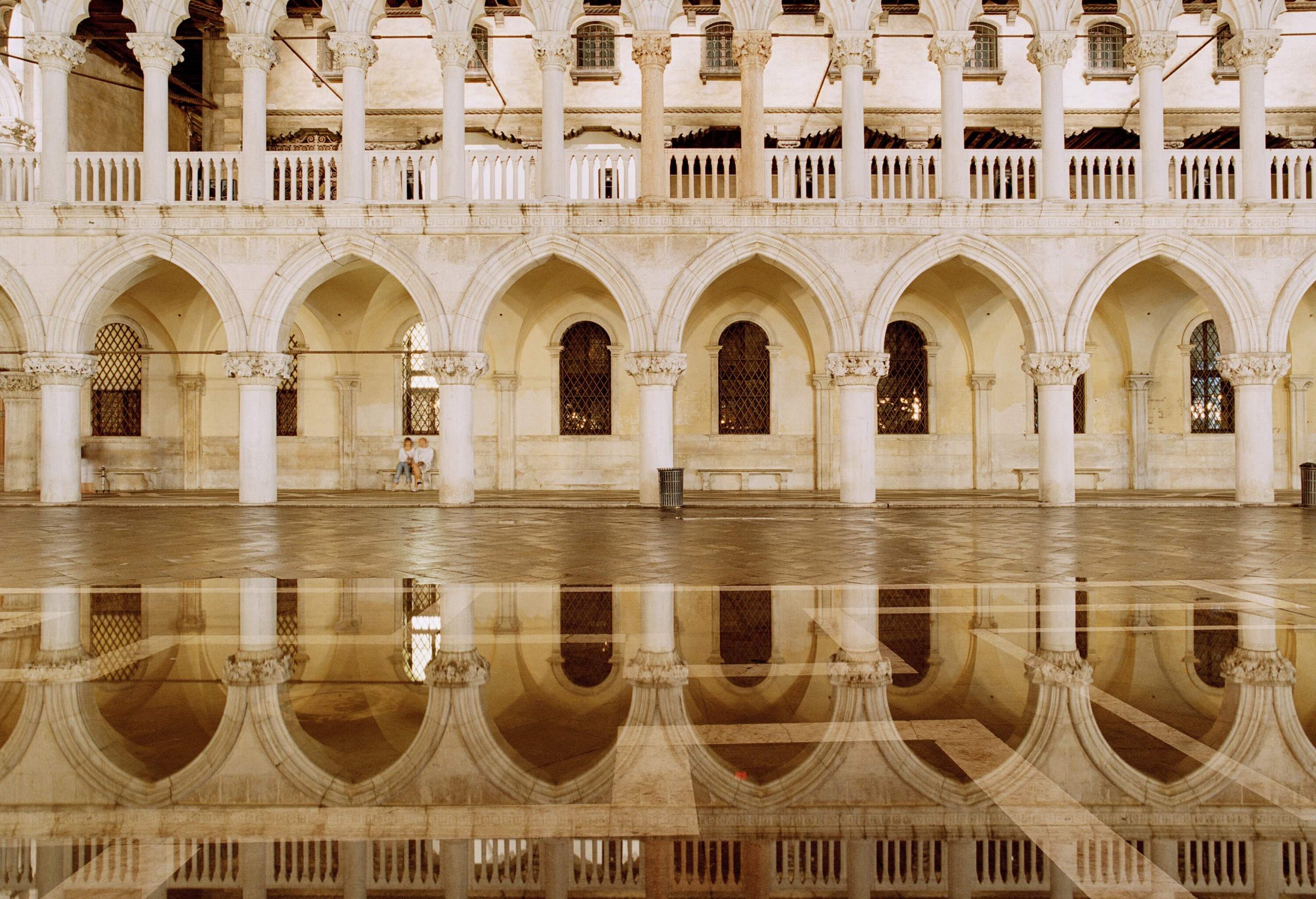 A wet floor reflects the image of a pillared archway and a pillared balcony with clover-shaped details.