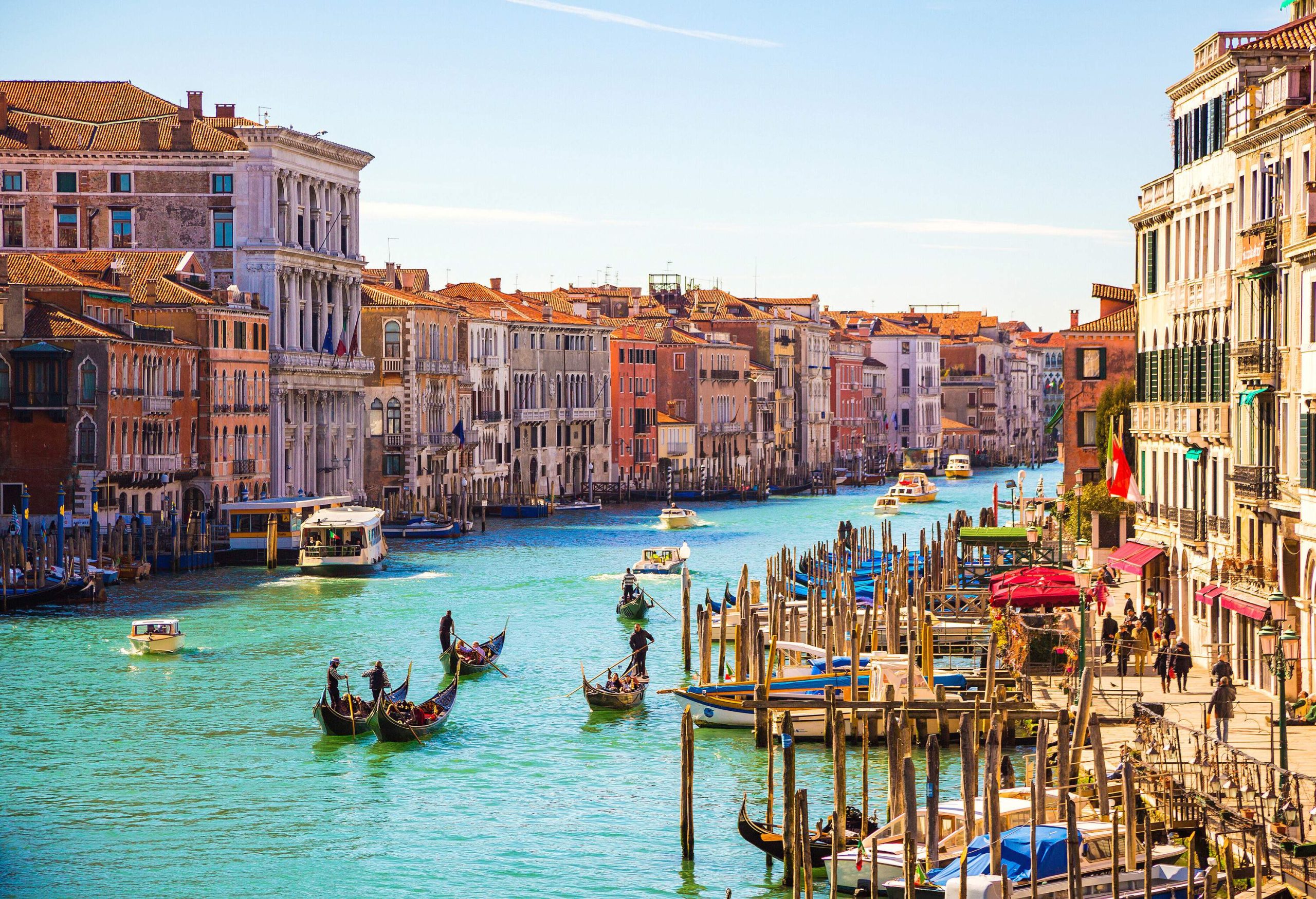 A water canal along the adjacent buildings with anchored boats and cruising gondolas and ferries.