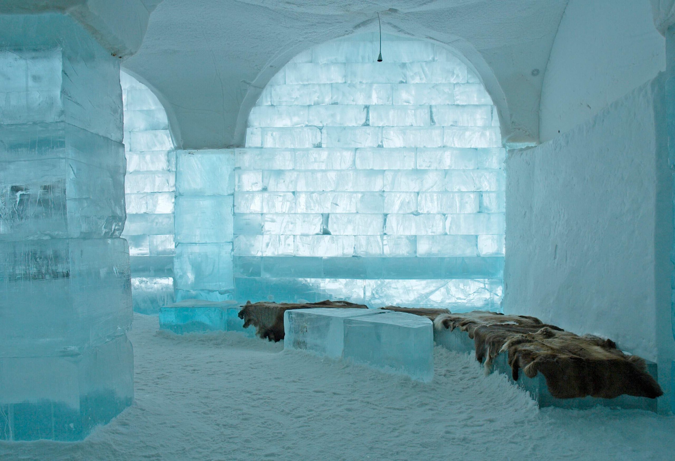 The inside of an ice hotel with intricate ice sculptures, beds and chairs made entirely of ice.