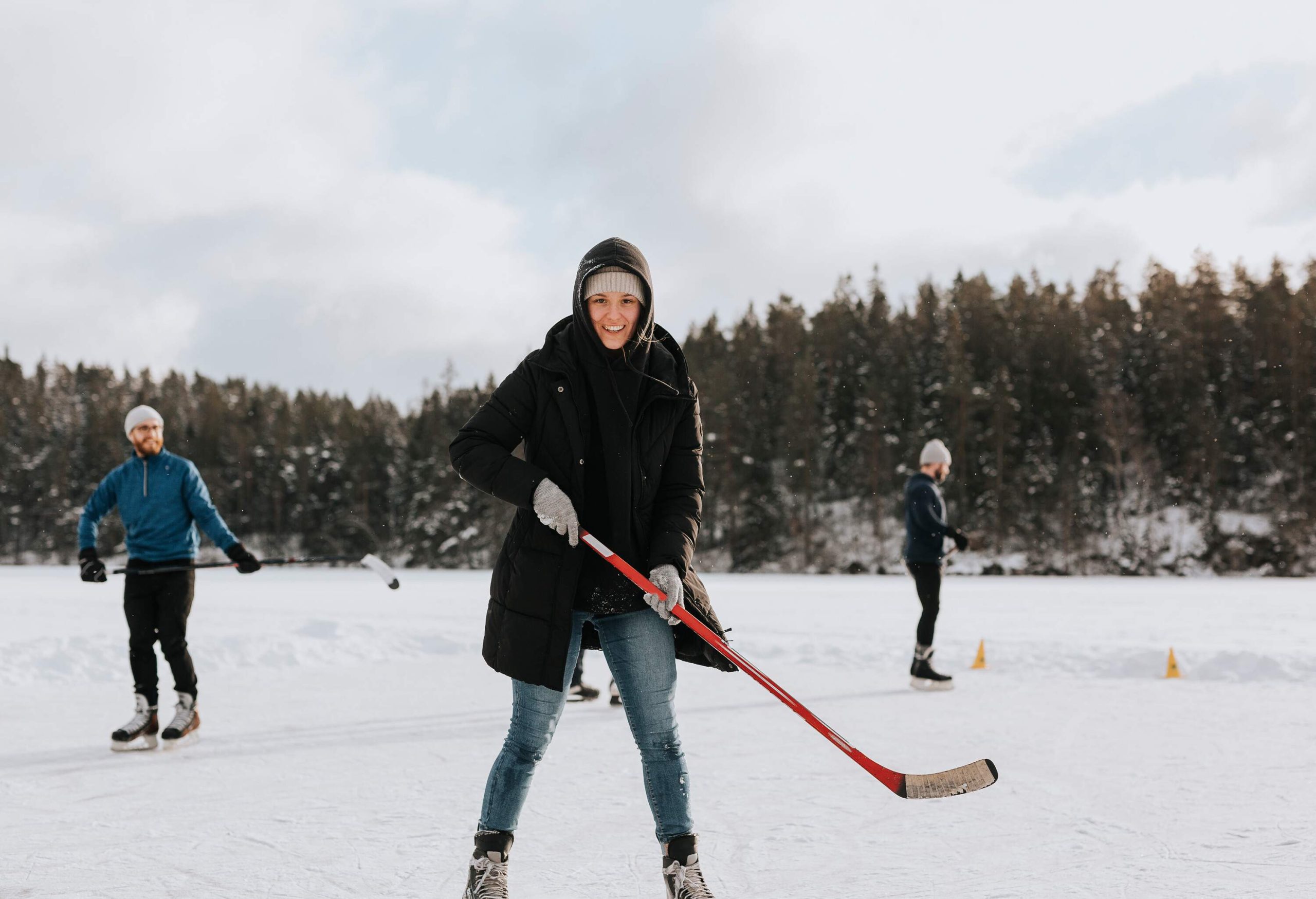 Three people dressed for the winter are skating and playing ice hockey on a frozen lake.