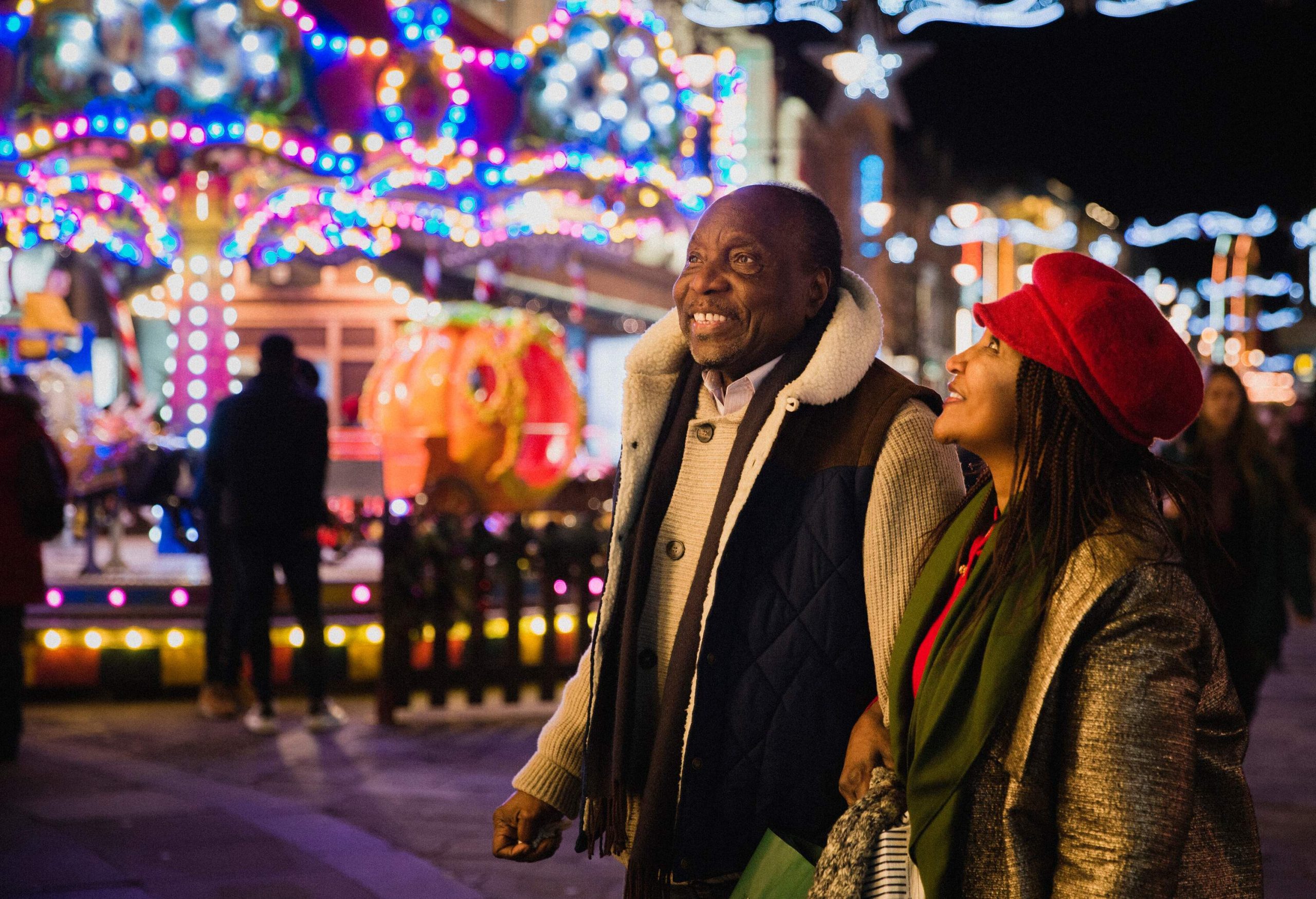 A side-view shot of a senior couple standing together next to the Christmas markets, they have been shopping for Christmas gifts on a cold December​ night.