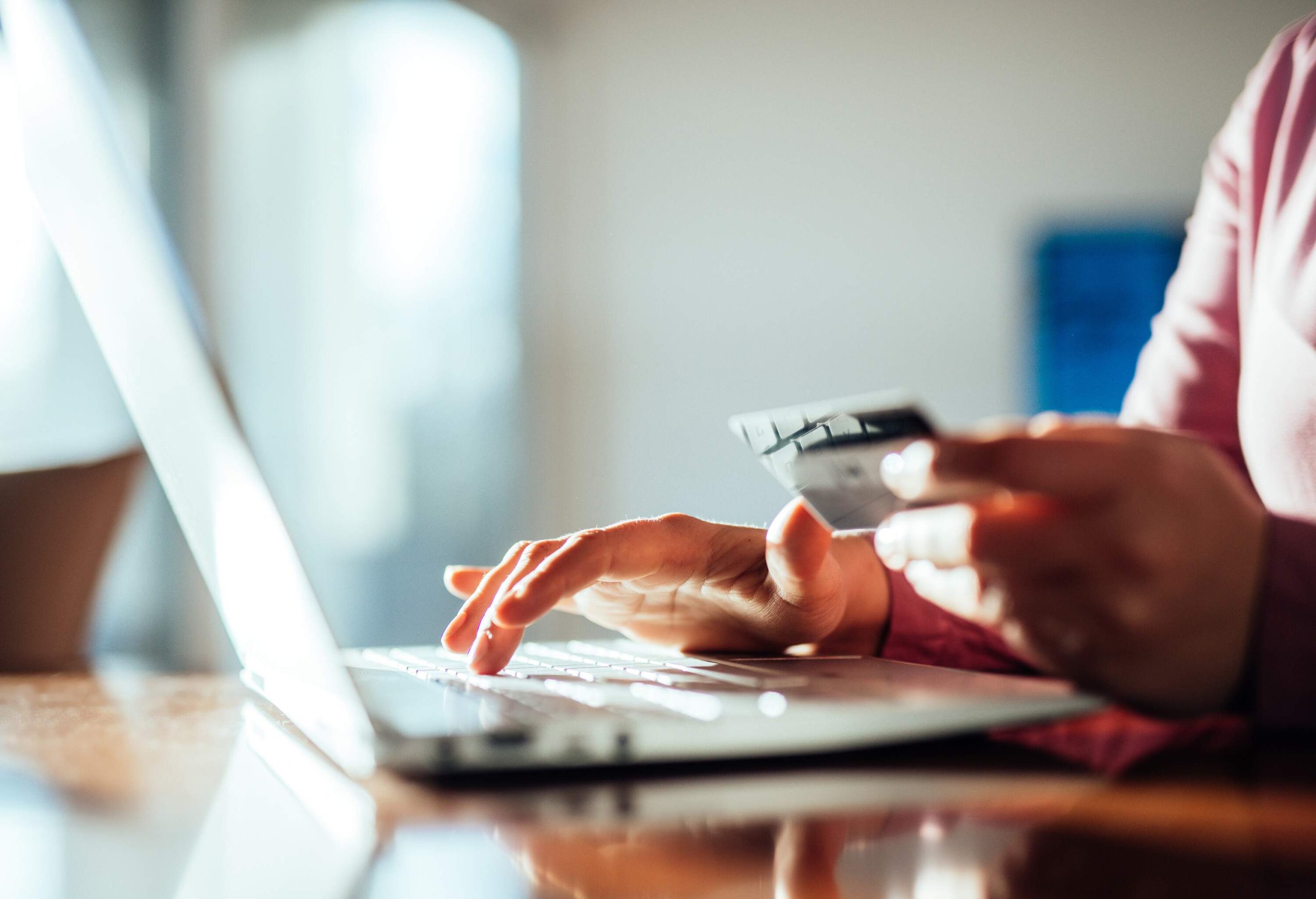 The right hand types on a laptop while the left hand holds a credit card.