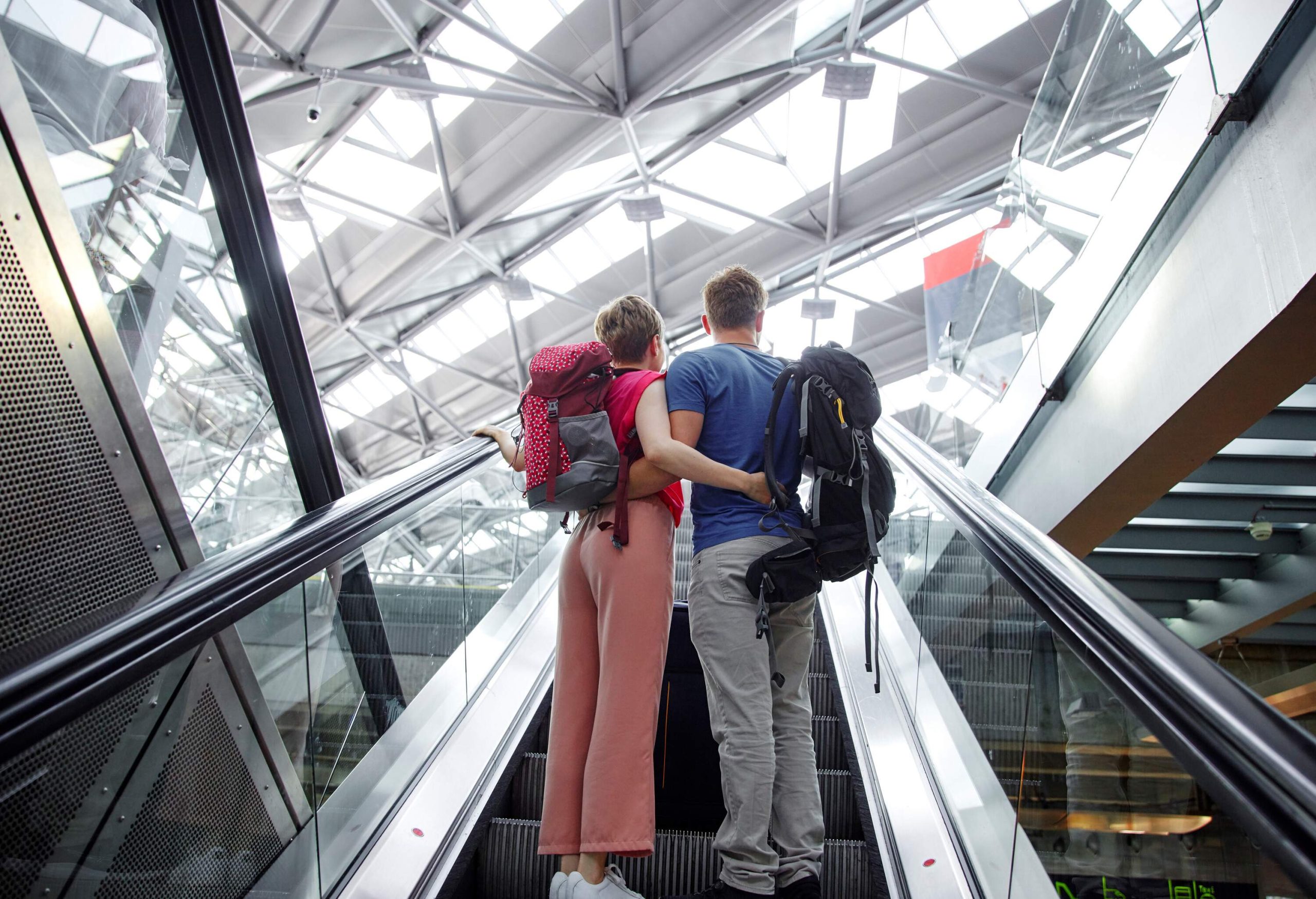 A couple with backpacks riding the escalator to the upper level of the terminal.