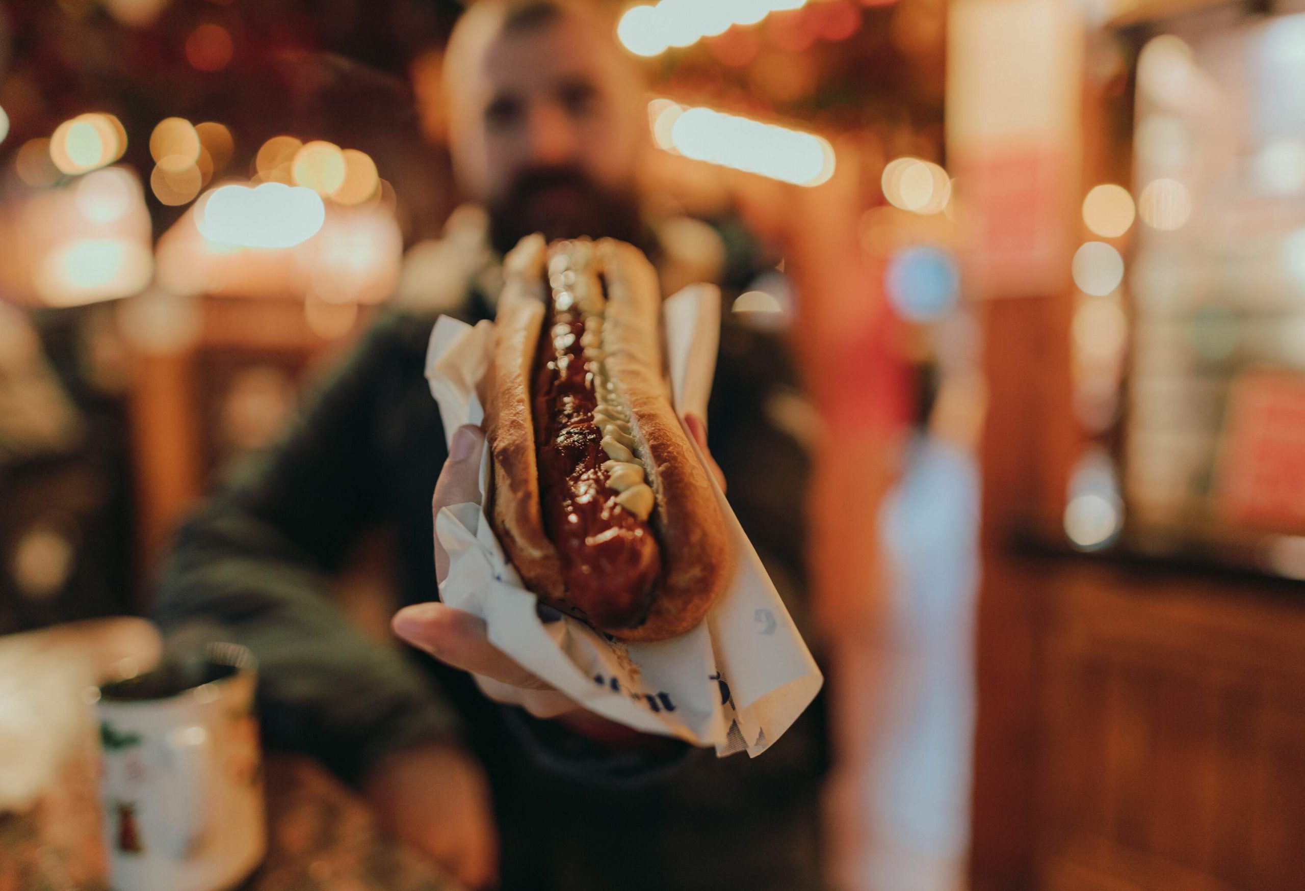 A man shows a bread bun with hotdog and mayonnaise.
