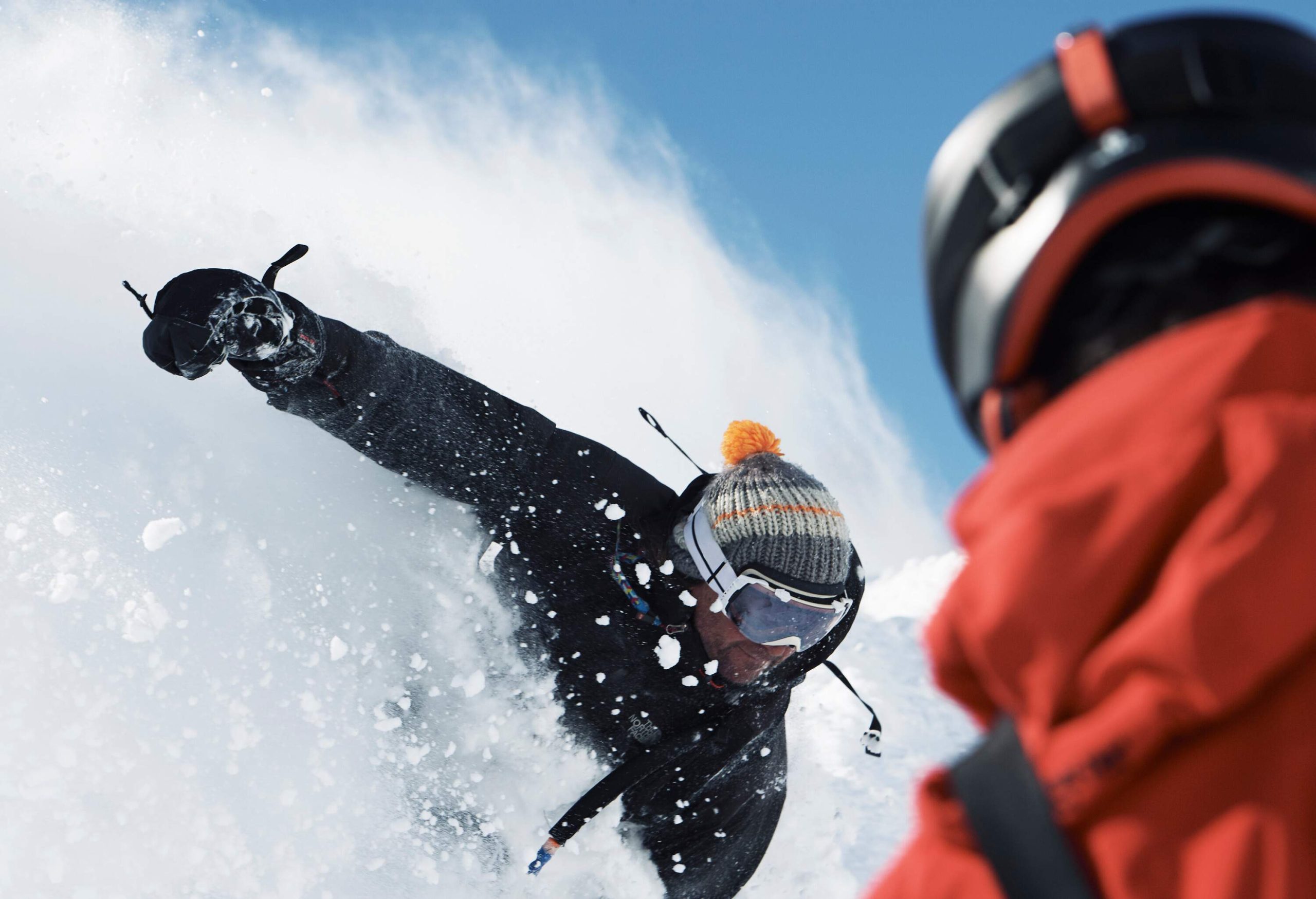 Two male skiers deep in powder snow splash. 