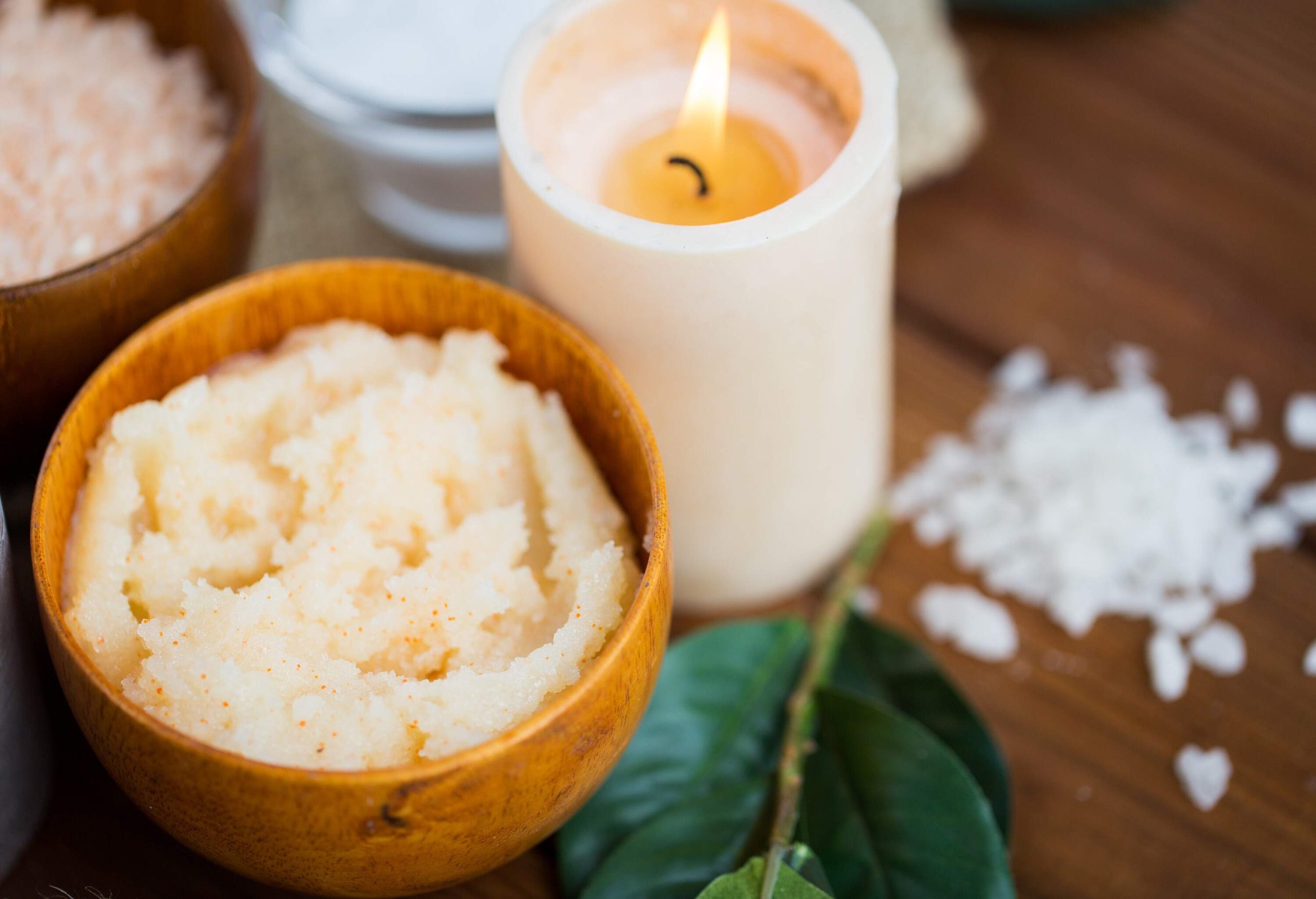 A lit candle is next to a small bowl filled with a body scrub.