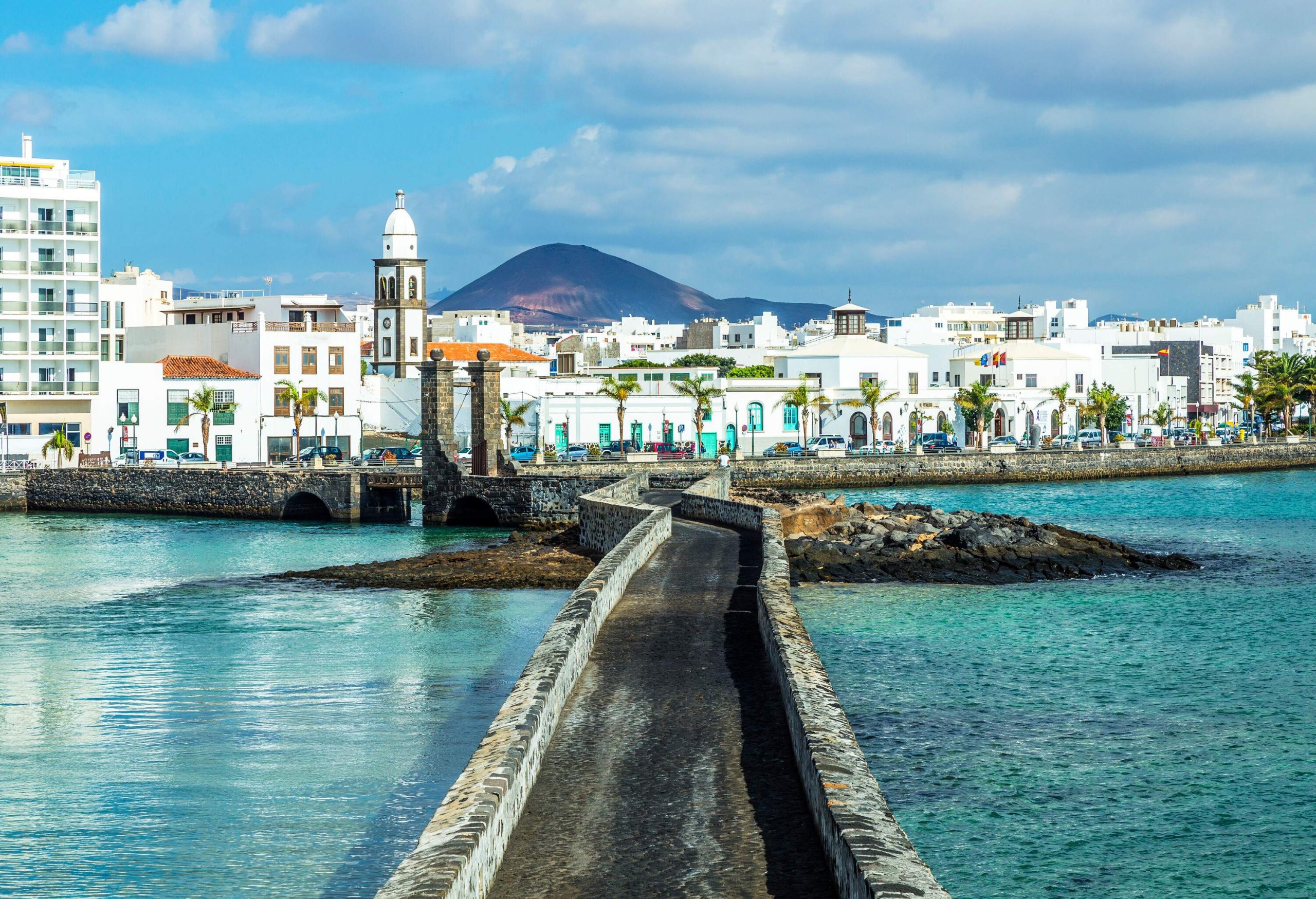 Beautiful cityscape with white houses, a mountain in the background, and a stone road leading down to the water.