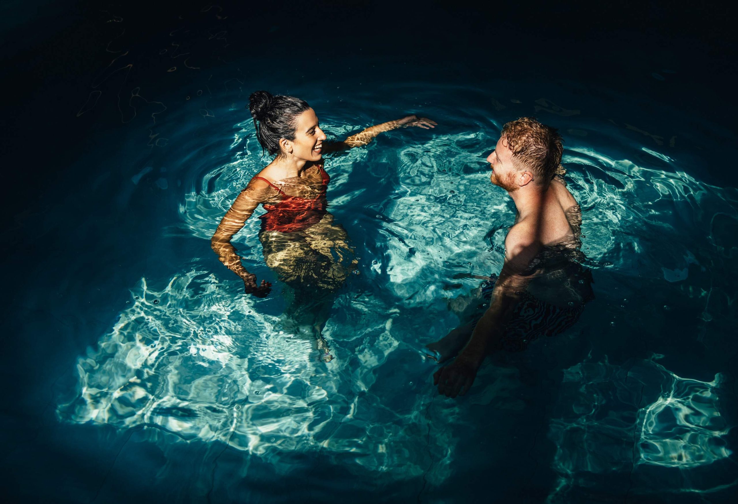 Smiling girlfriend and boyfriend in swimwear talking together in the swimming pool