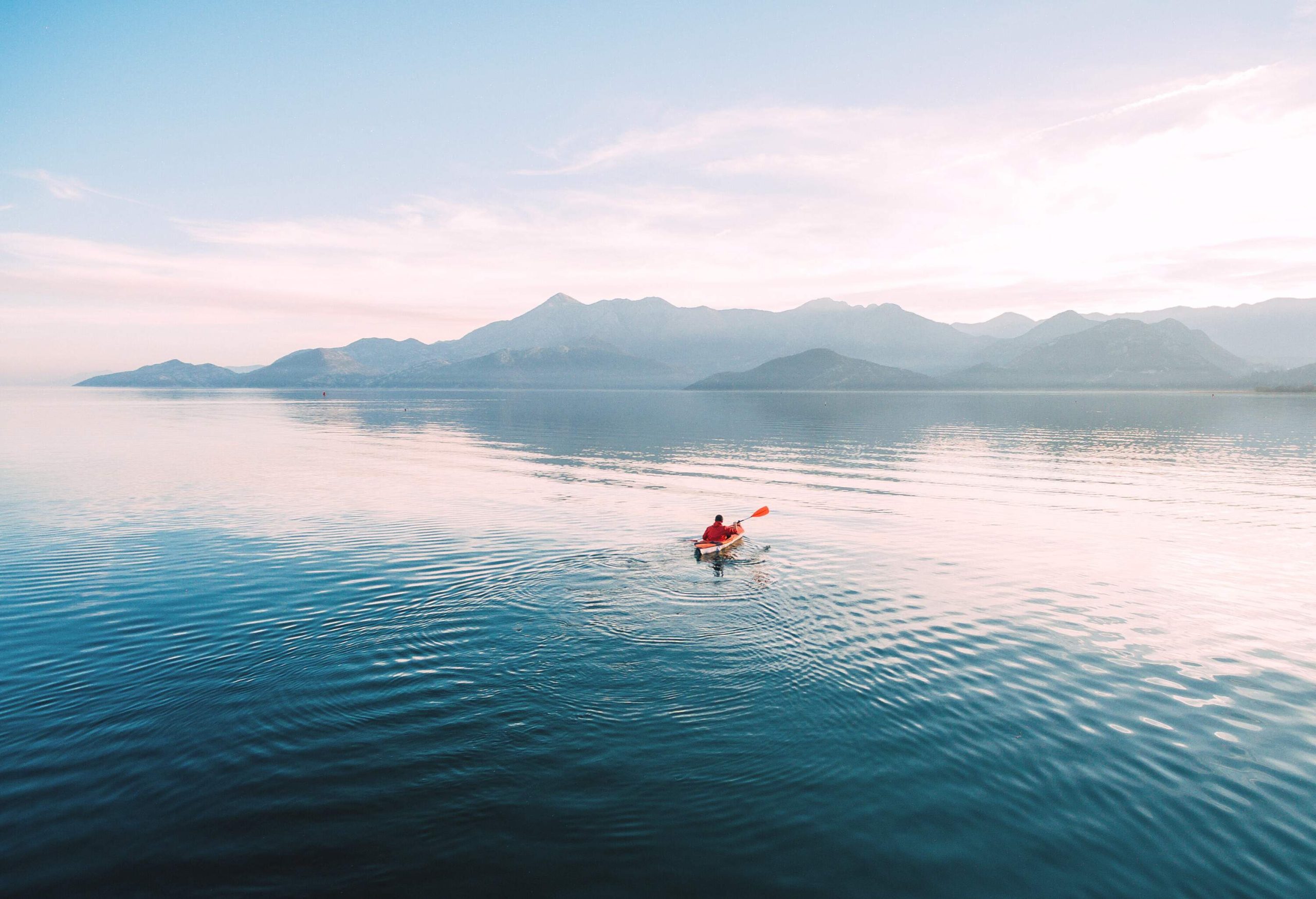 A man paddling gently in the middle of a calm lake towards the surrounding mountains.