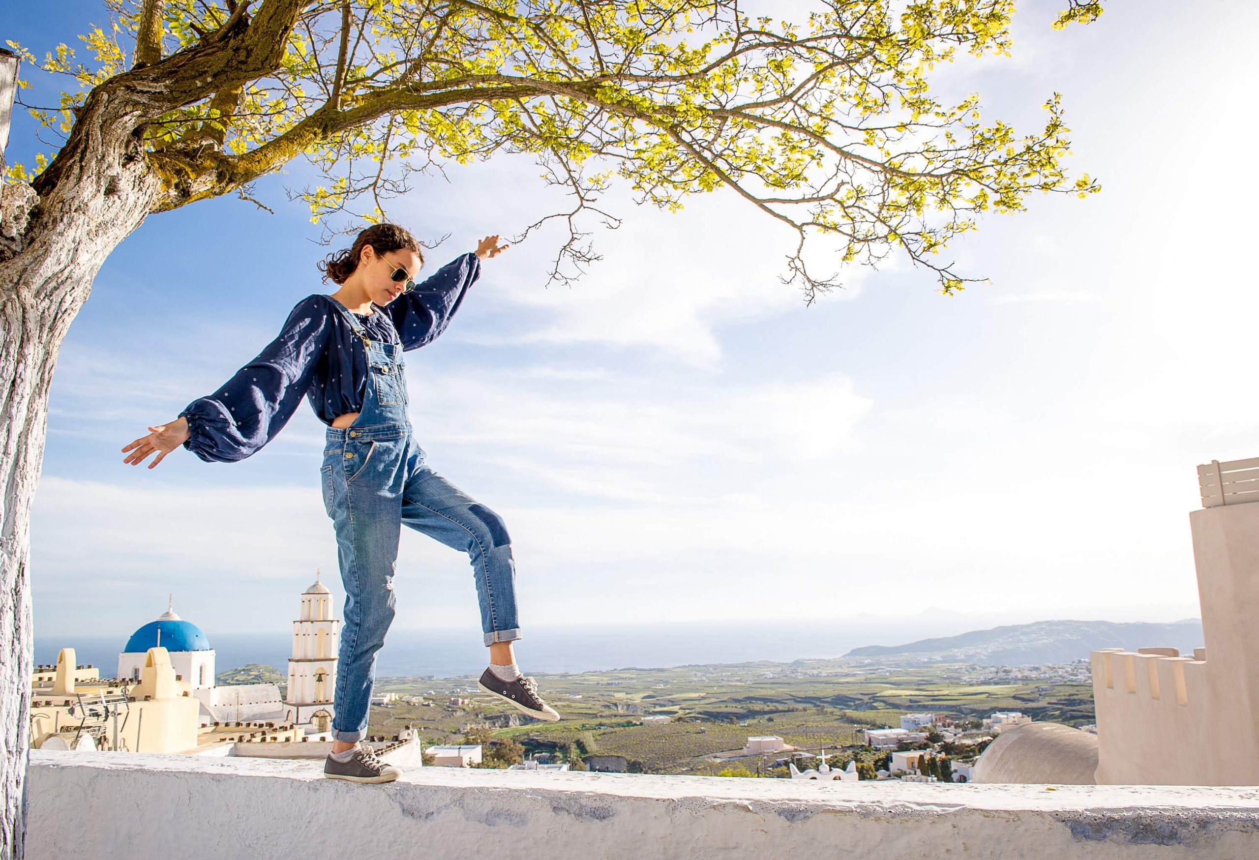 A person donning sunglasses stands on the edge, skillfully balancing while overlooking the expansive landscape and taking in the breathtaking views that stretch before them.