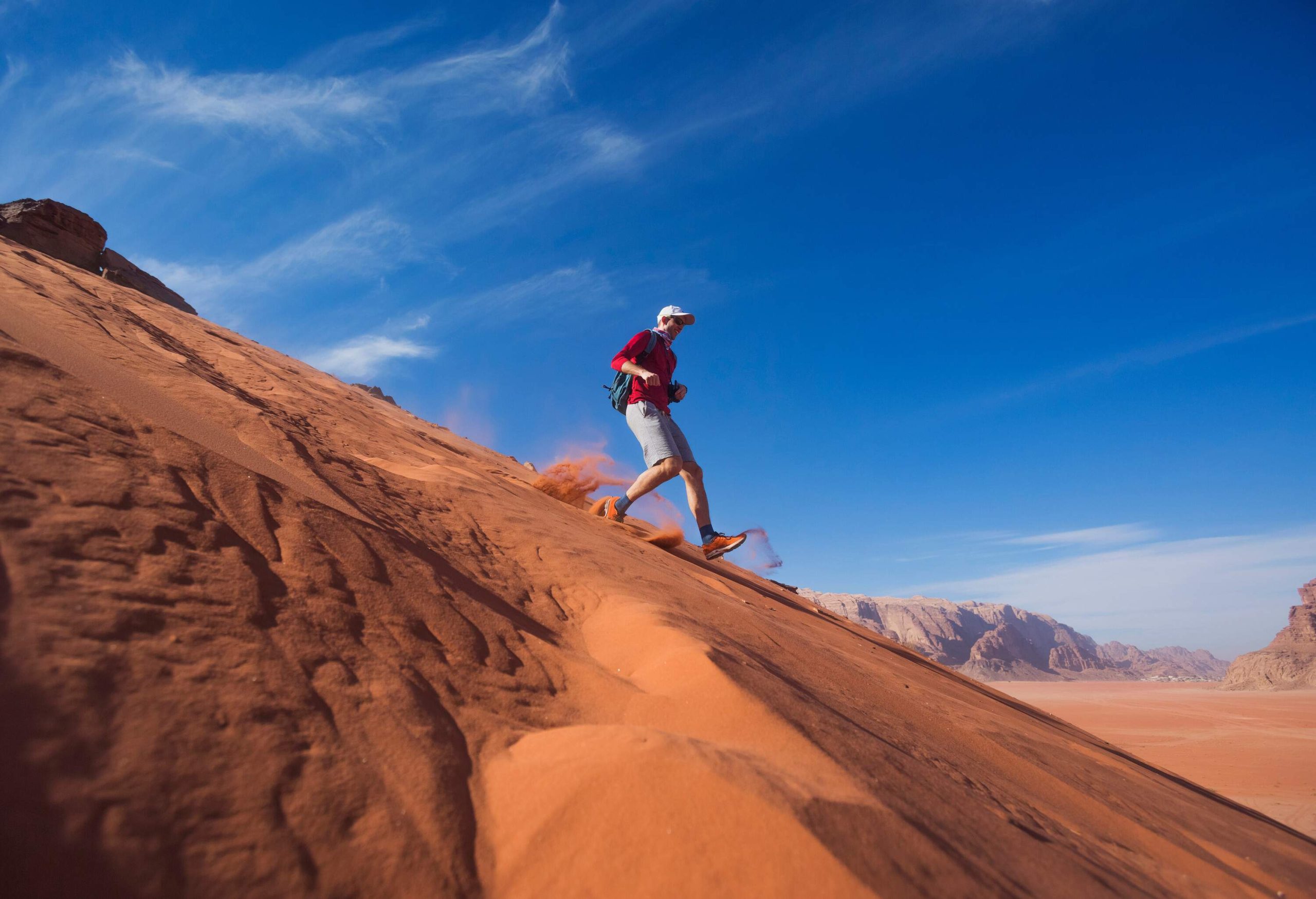 A man sprints down the sandy dune in the desert.