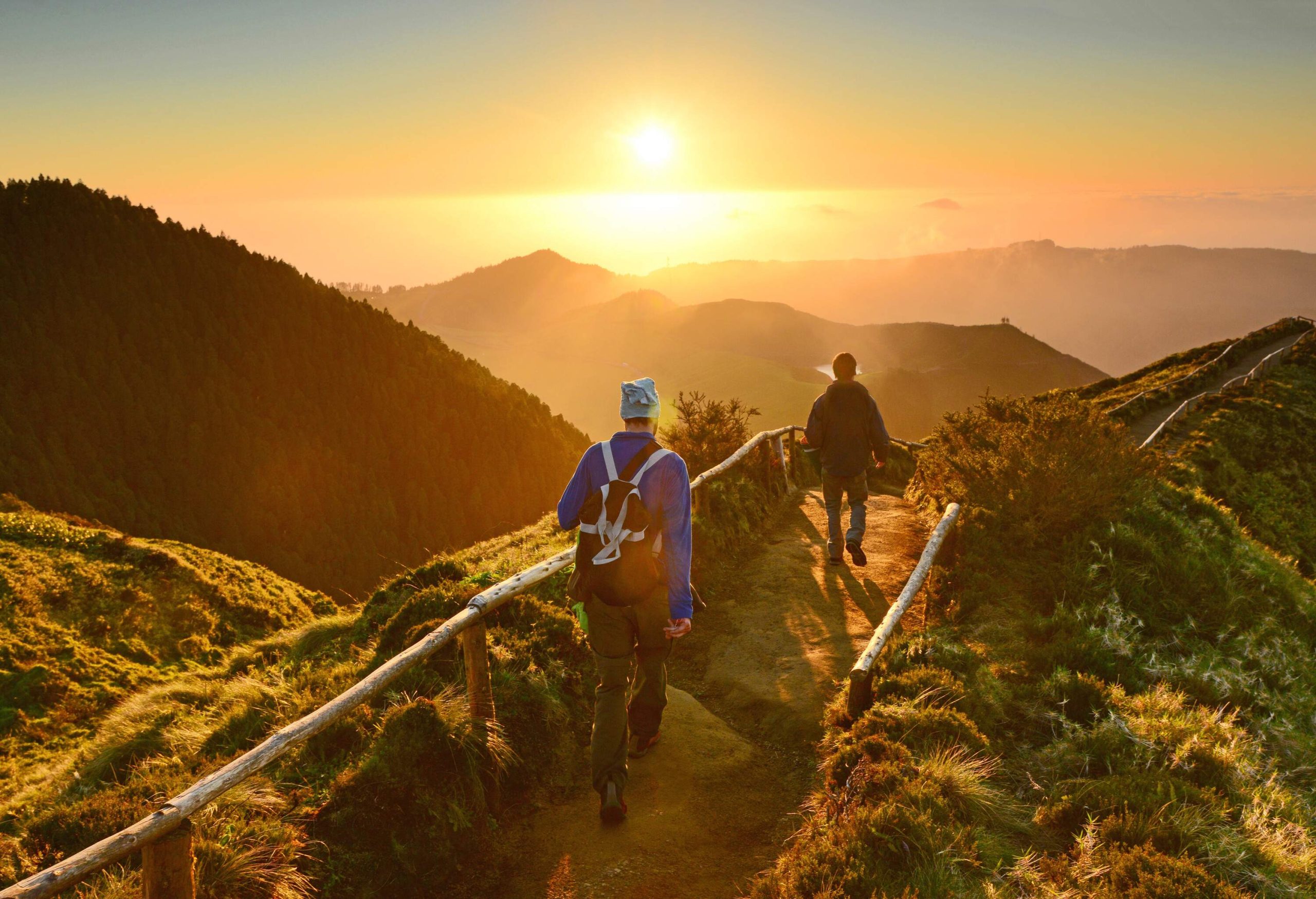 Two individuals on a trail overlooking the silhouette of mountains at sunrise.